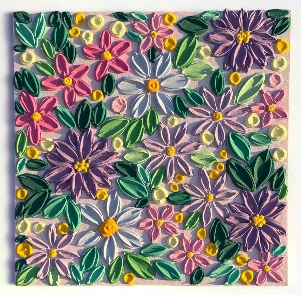 Colorful quilt with hand-stitched floral design featuring pink, purple, white, and lavender flowers, green leaves, and yellow accents on a fabric background.