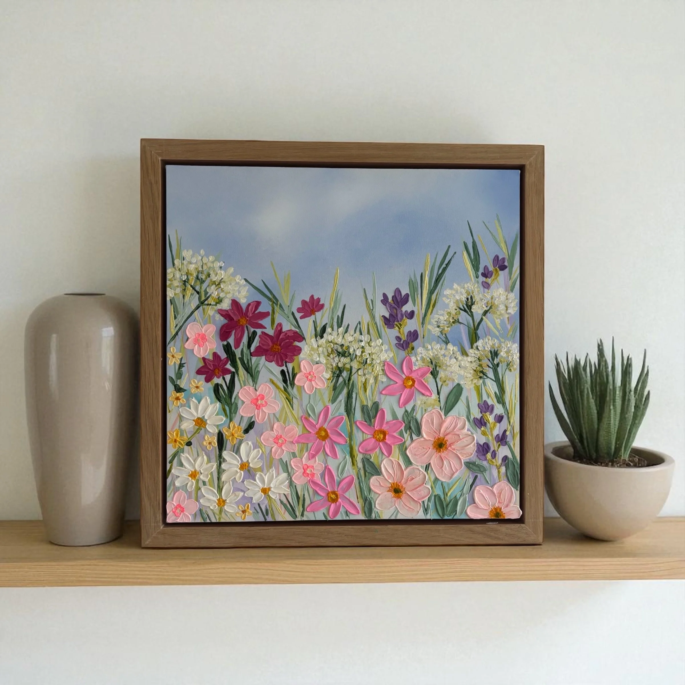 Framed painting of colorful flowers and greenery on a wall, flanked by two white vases on a wooden shelf.
