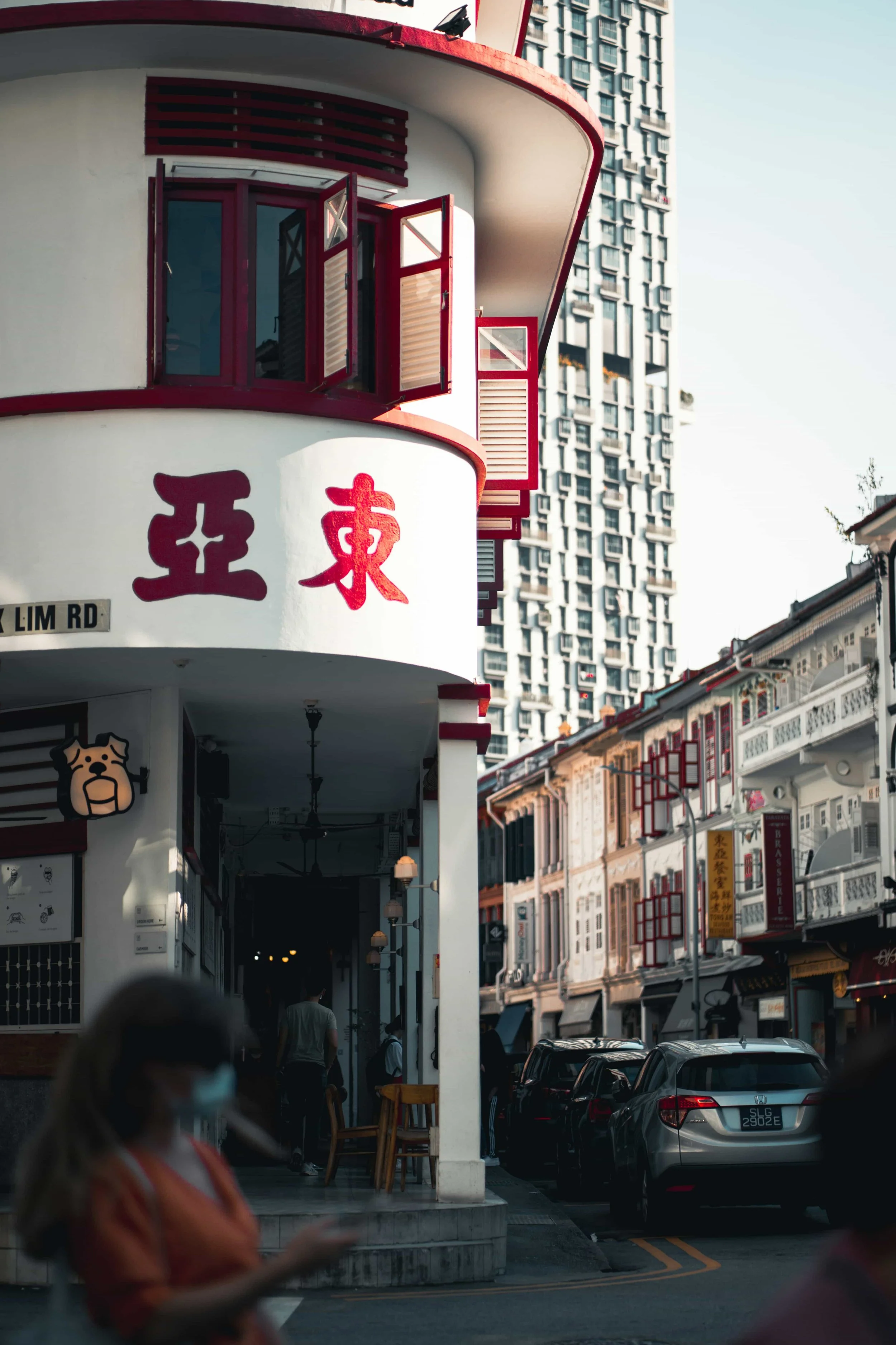 Singapore Street scene with buildings and a restaurant featuring red Chinese Wayfinding accents; people walking, cars parked, and high-rise in background.