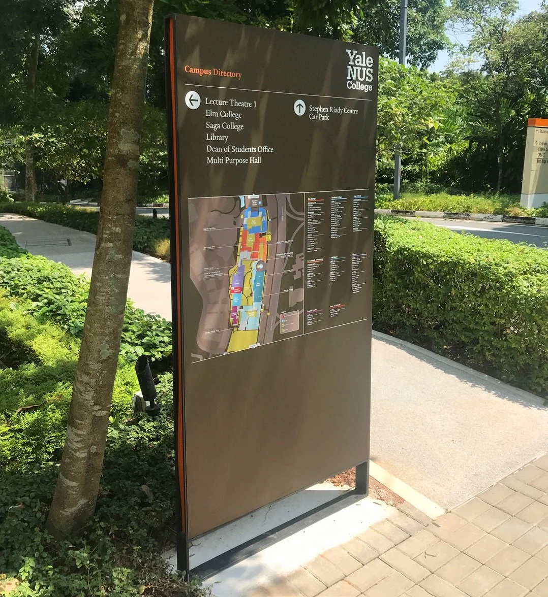 Yale NUS College campus map and wayfinding directory sign, standing on a sidewalk surrounded by greenery.