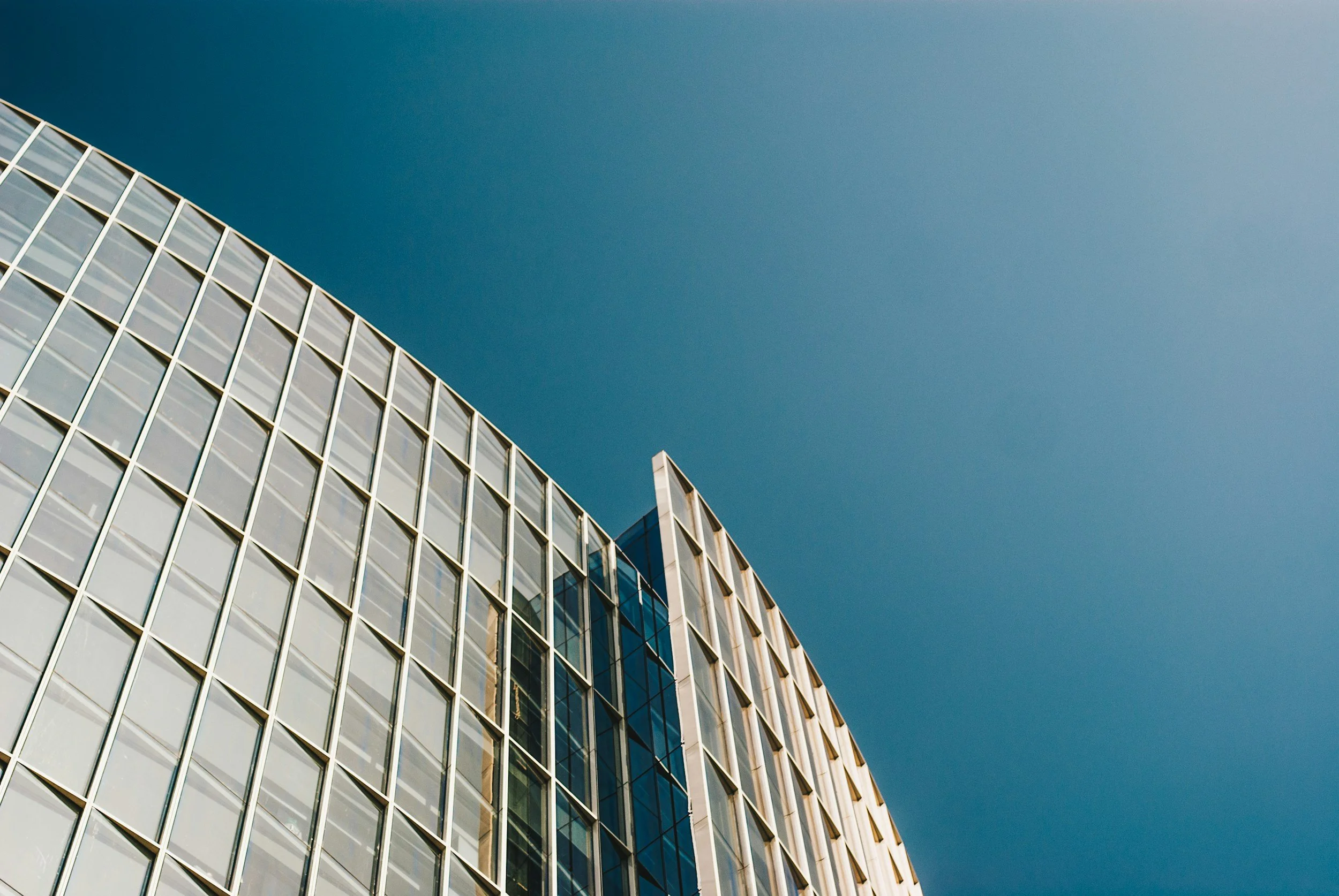 Modern glass building with a grid-like pattern of windows under a clear blue sky.