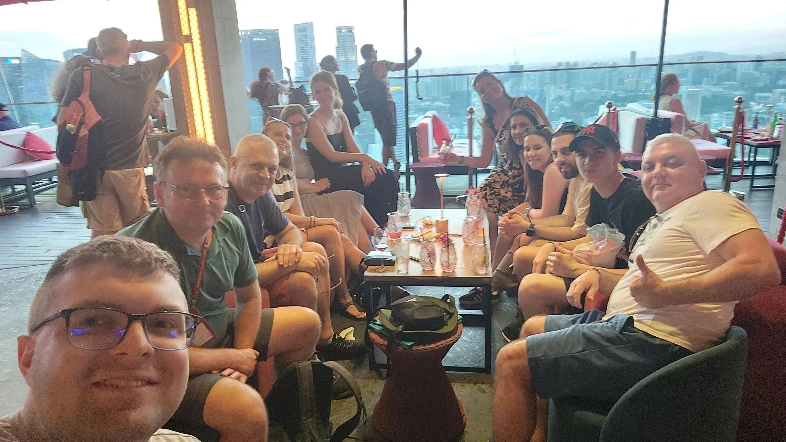 A group of people sitting at a long table in a restaurant with a city skyline view in the background.