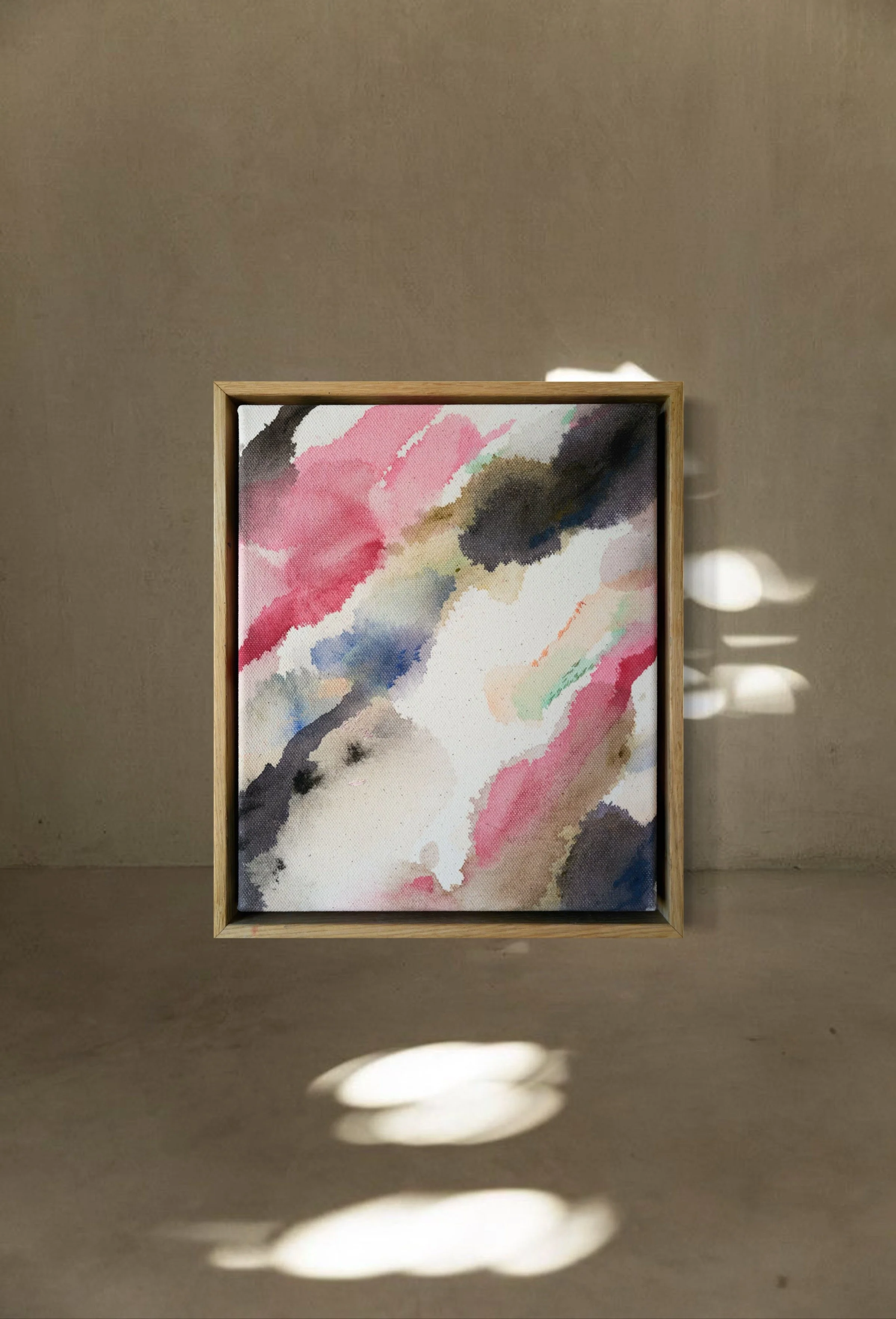 Abstract watercolor painting with pink, black, beige, and blue colors in a wooden frame, illuminated by sunlight creating shadow patterns on a beige wall and floor.