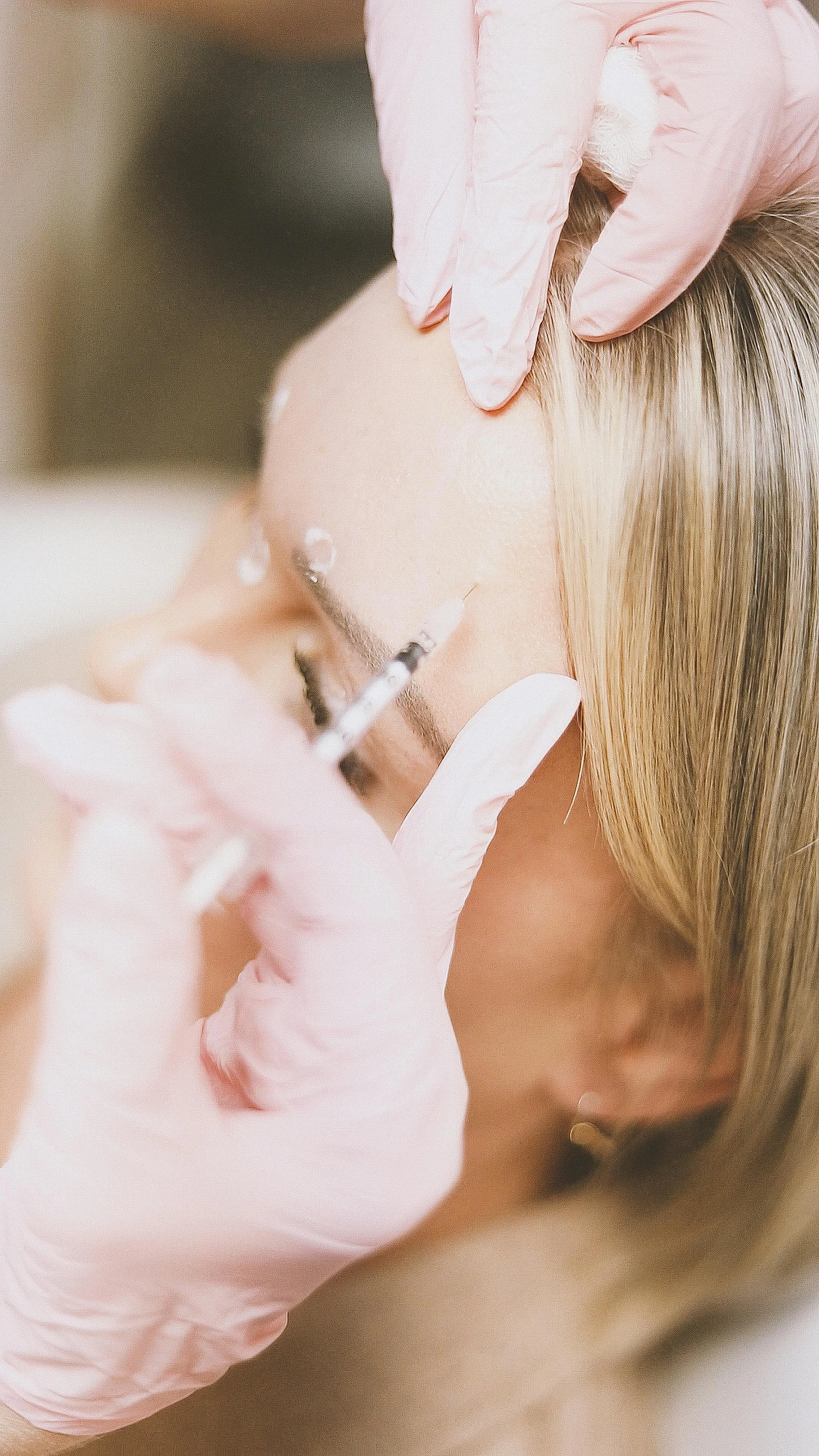 Person receiving a cosmetic injection in the face from a healthcare professional wearing pink gloves.