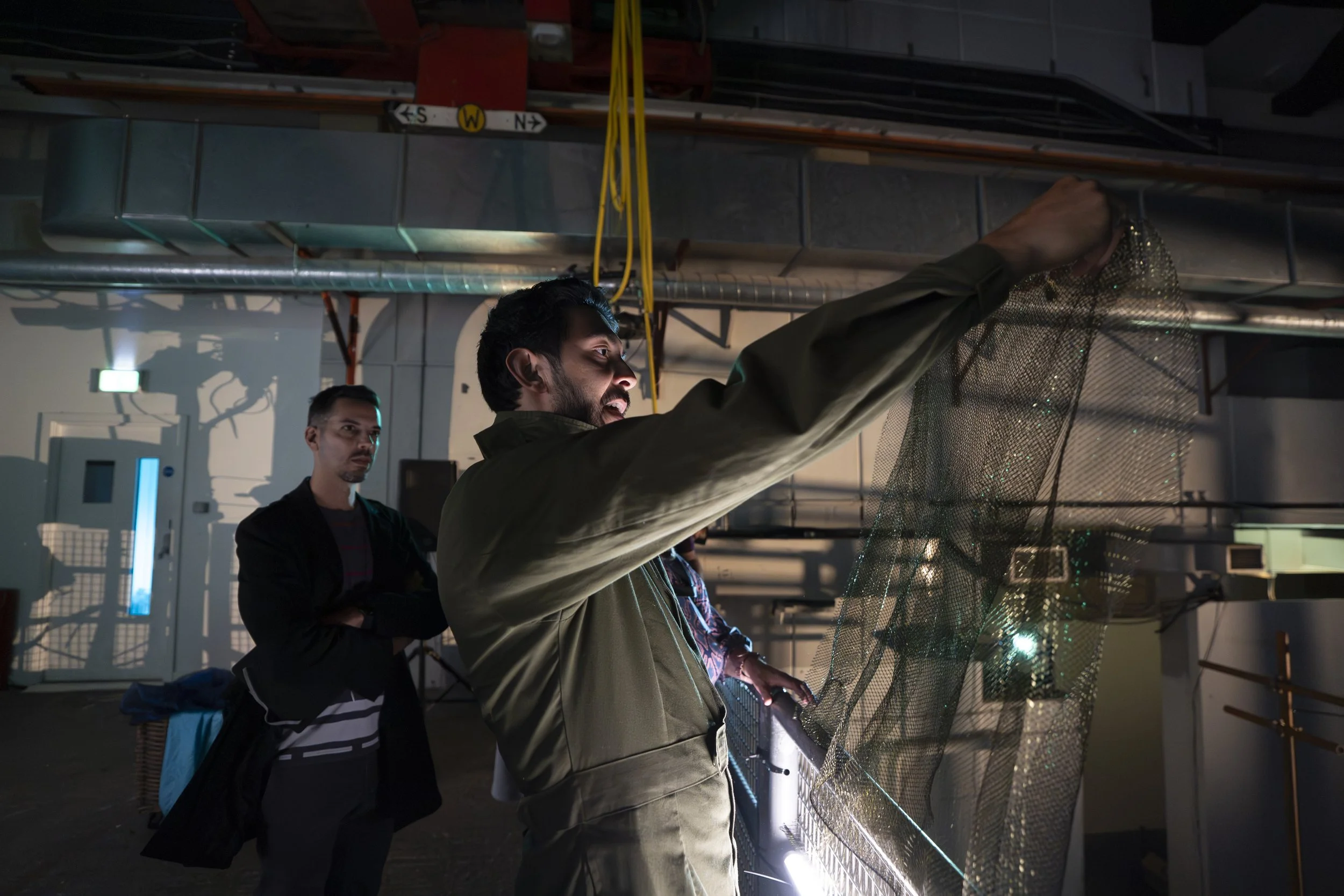 People working on a project involving a mesh structure in an industrial or workshop setting.