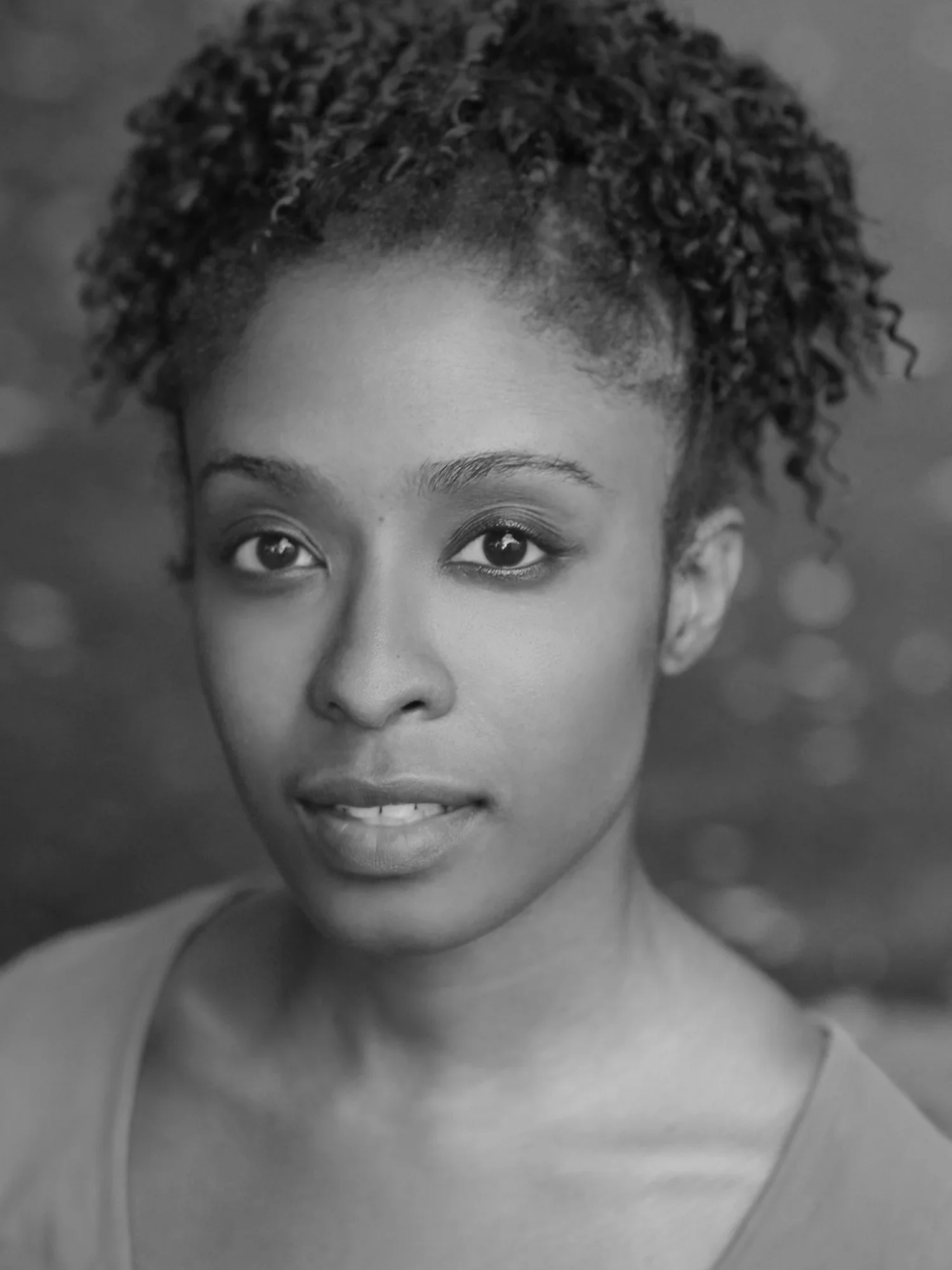 Close-up black and white photo of a woman's face with natural curly hair, partially visible, with her eyes and lips showing.