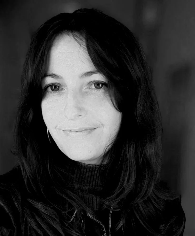 Black and white portrait of a woman with shoulder-length dark hair, wearing a turtleneck and a jacket, smiling softly at the camera.