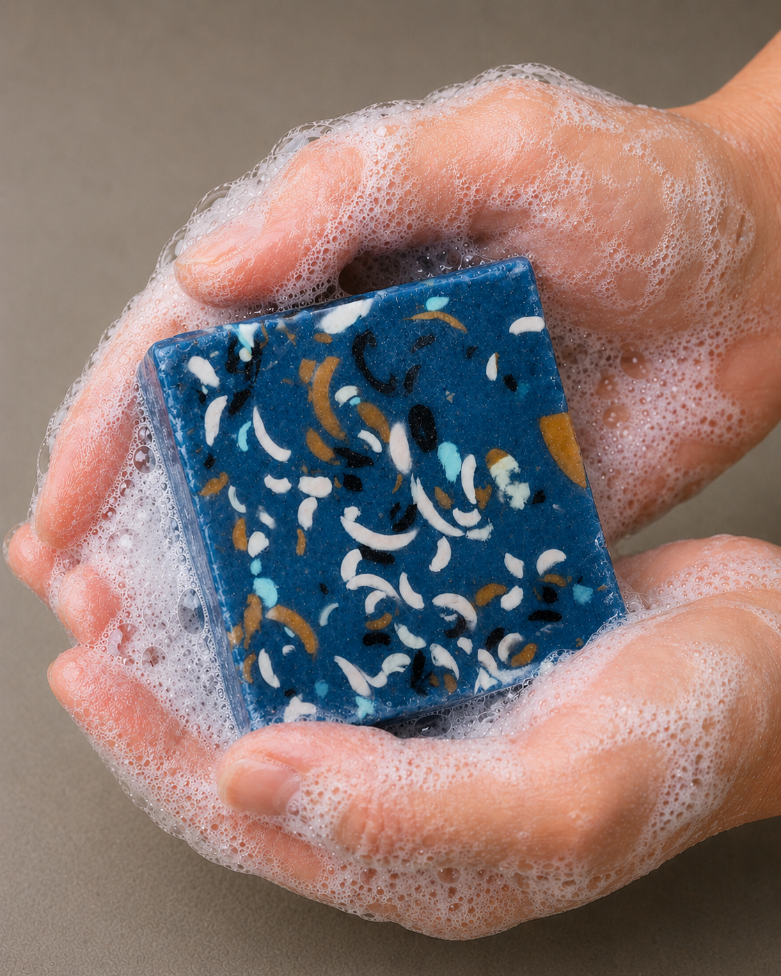 Person washing hands with a square blue and multicolored soap with bubbles.