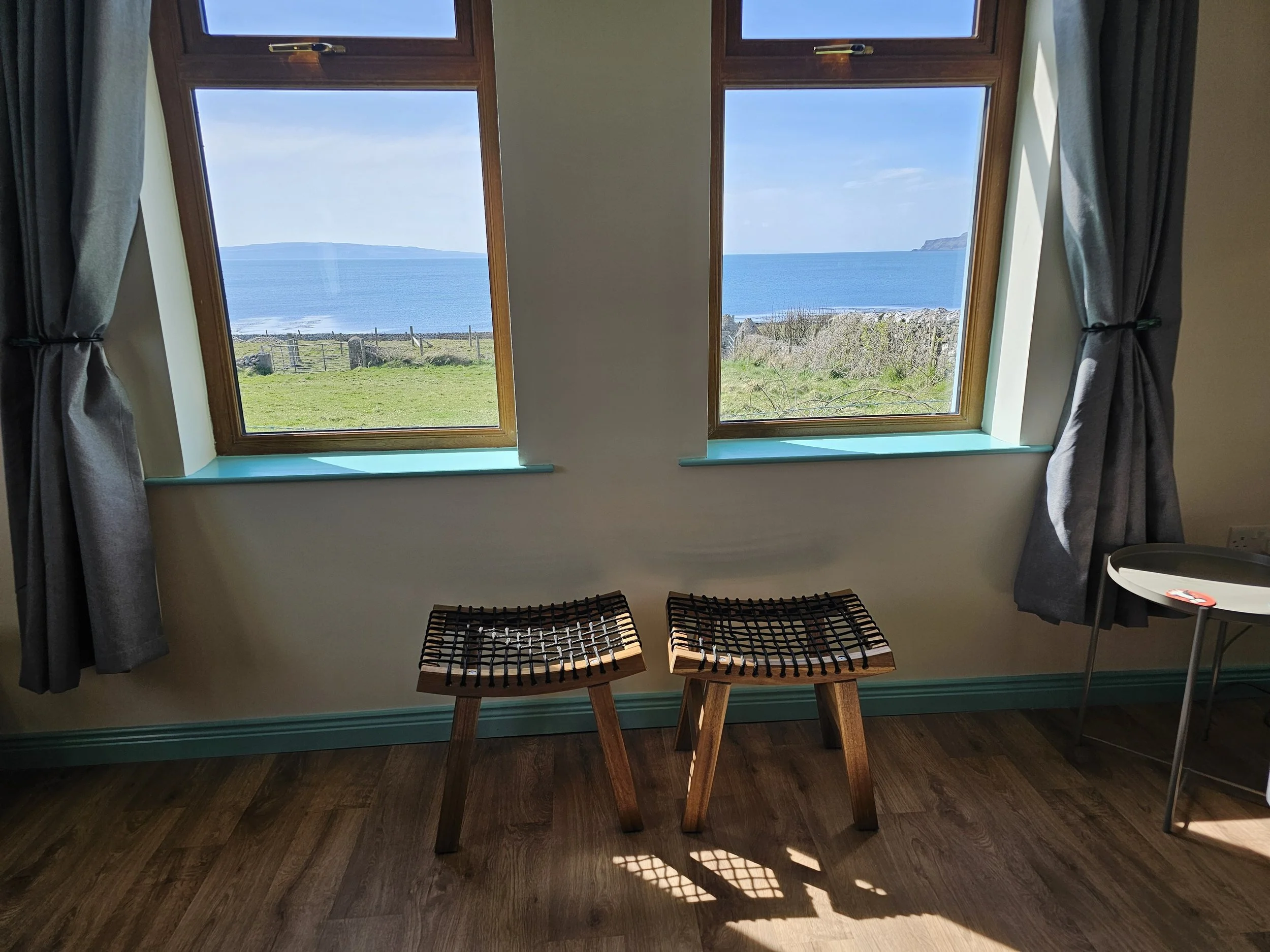 View through two windows showing a coastal landscape with blue sea, green grass, and cliffs in the distance