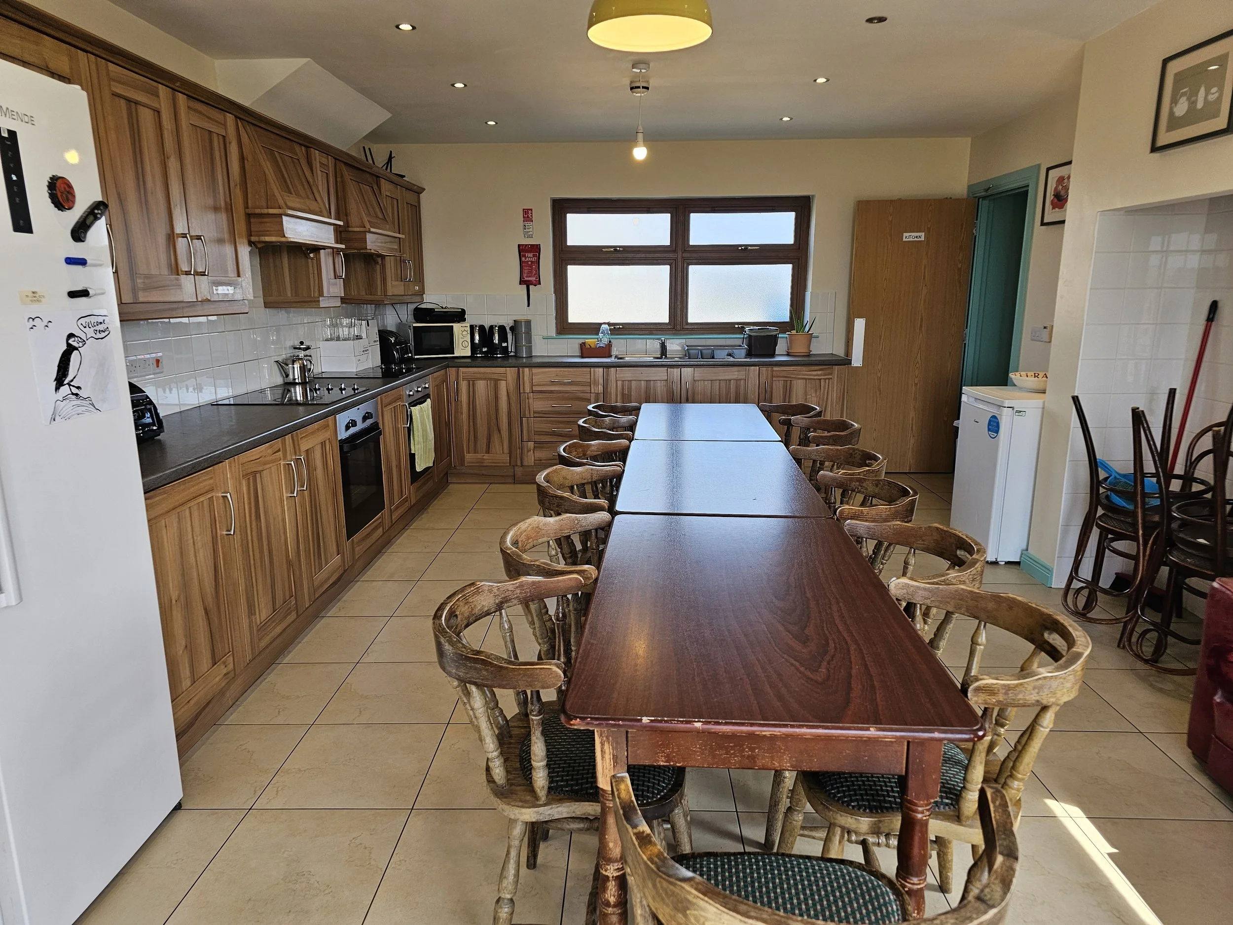 A kitchen with wooden cabinets, a table with wooden chairs, a window above the sink, and various appliances on the counter.