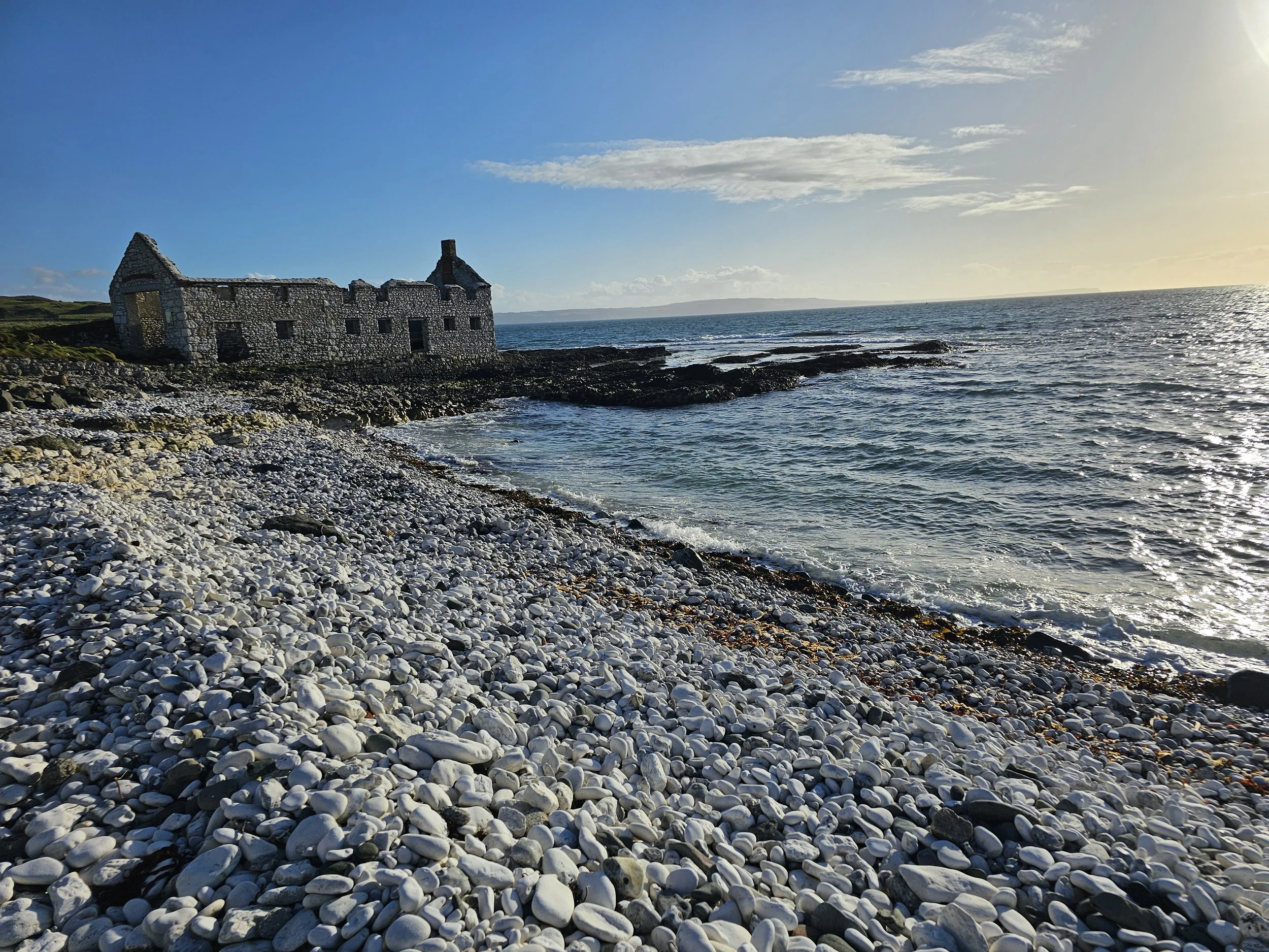 Ruined stone house on rocky coast with ocean and sky in the background