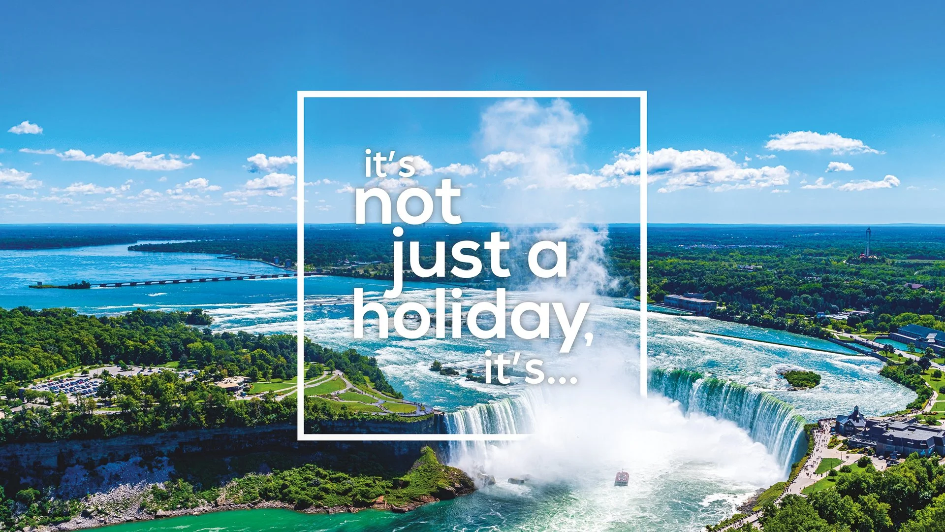 Aerial view of Niagara Falls with water pouring over the waterfalls, greenery, and a cityscape in the background with a blue sky and some clouds. Text overlay says, "it’s not just a holiday, it’s..."