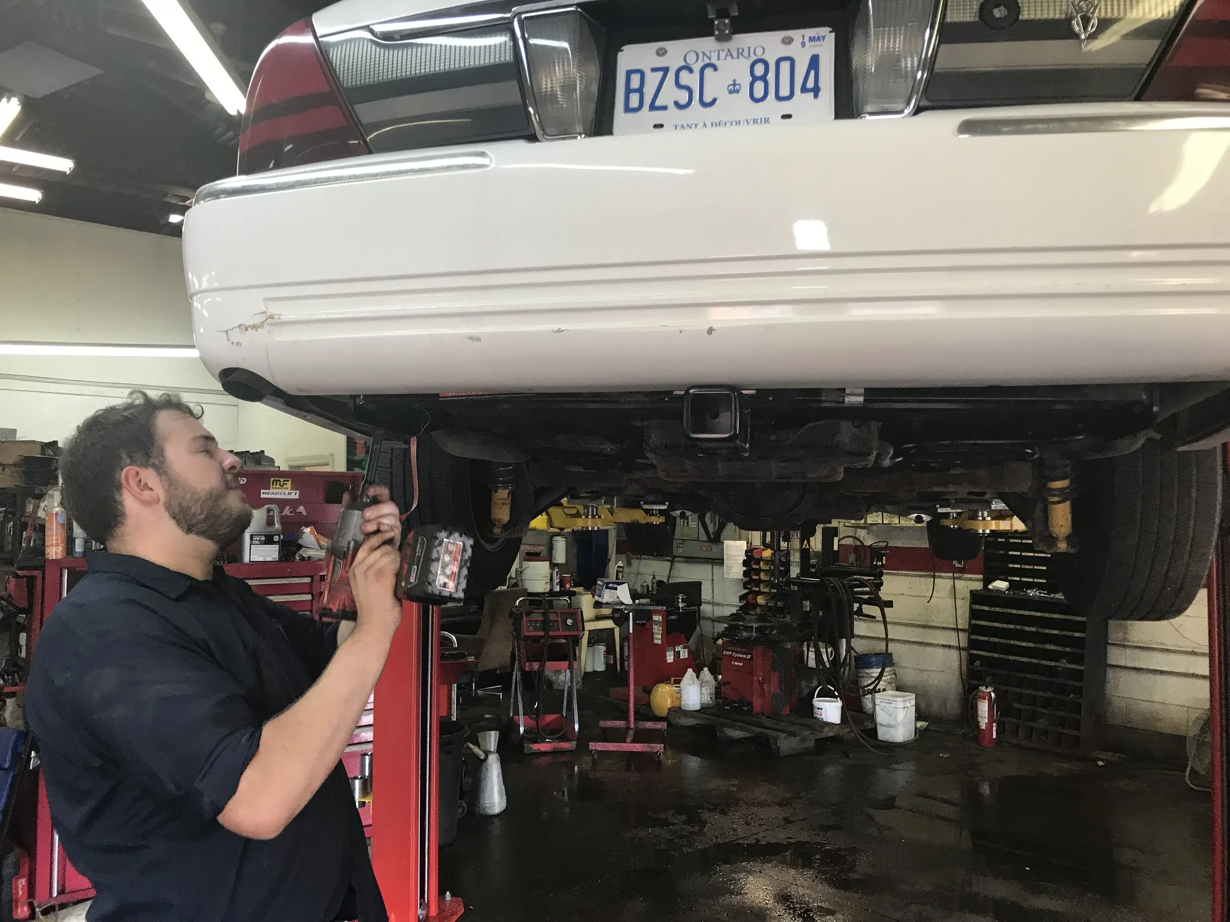Photo of a man working on the rear axle of a white car.