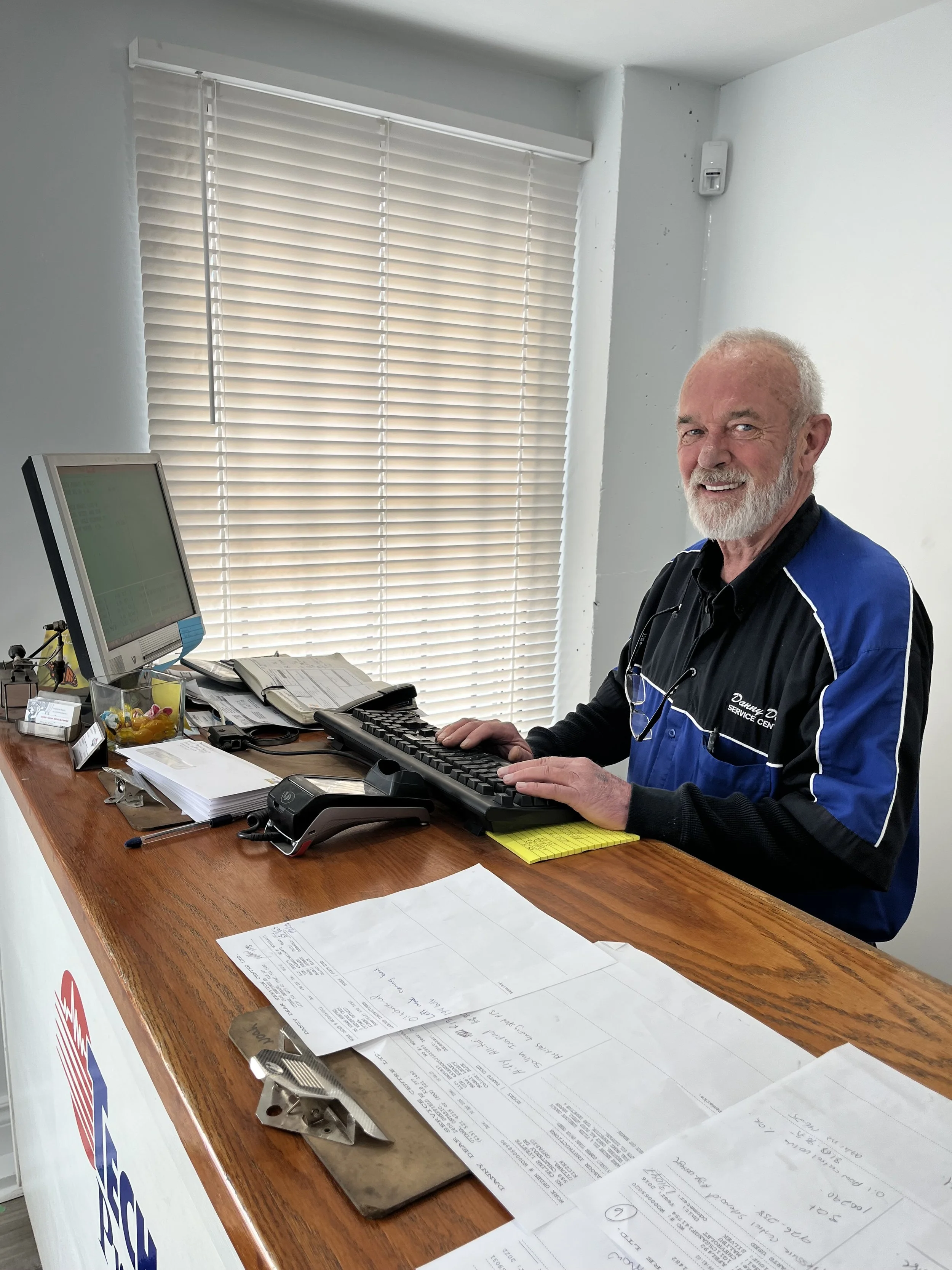 An older bearded man typing at a computer, while looking at the camera.