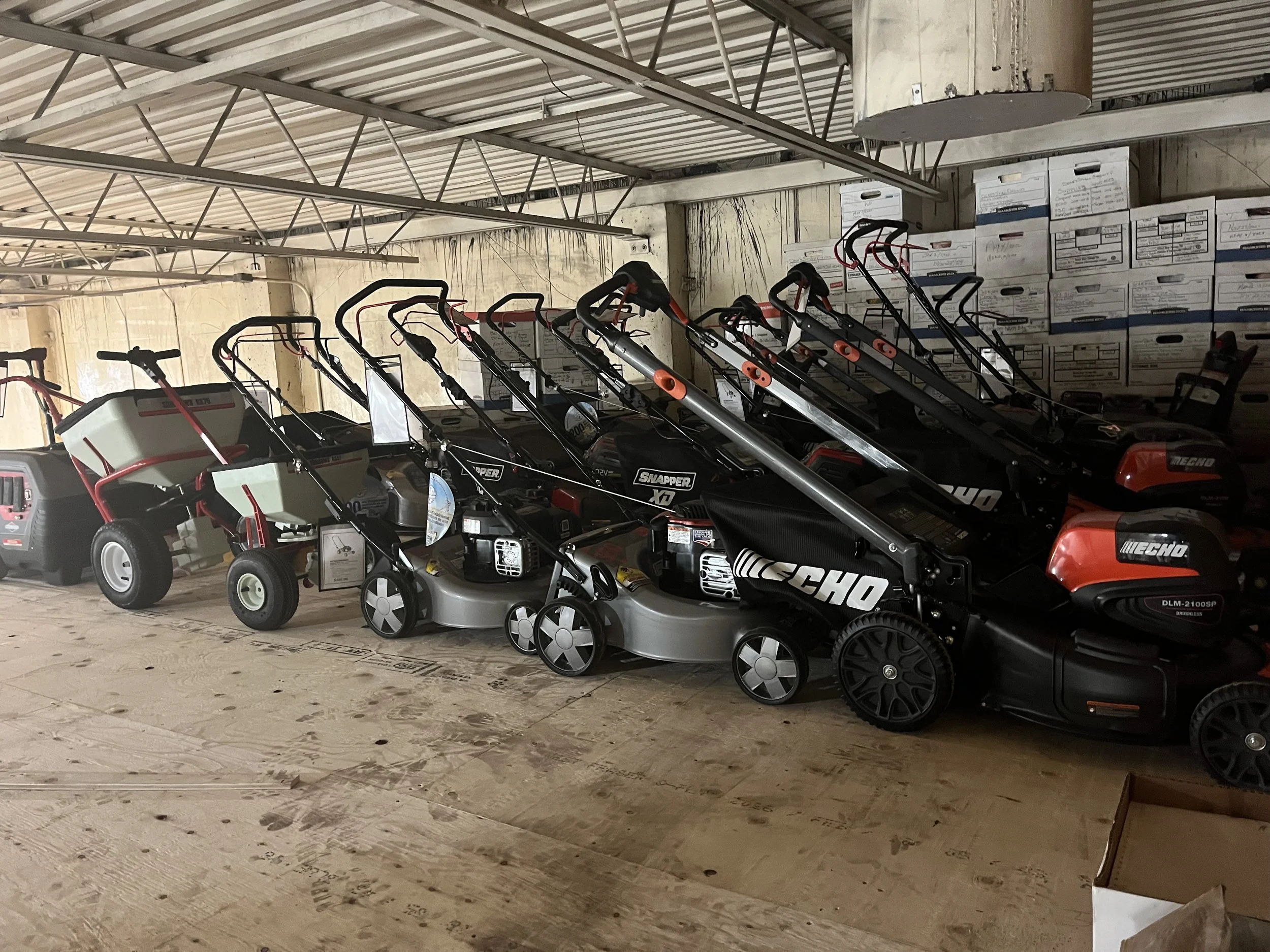 A storage area with lawnmowers, stacked boxes, and a metal ceiling with beams.
