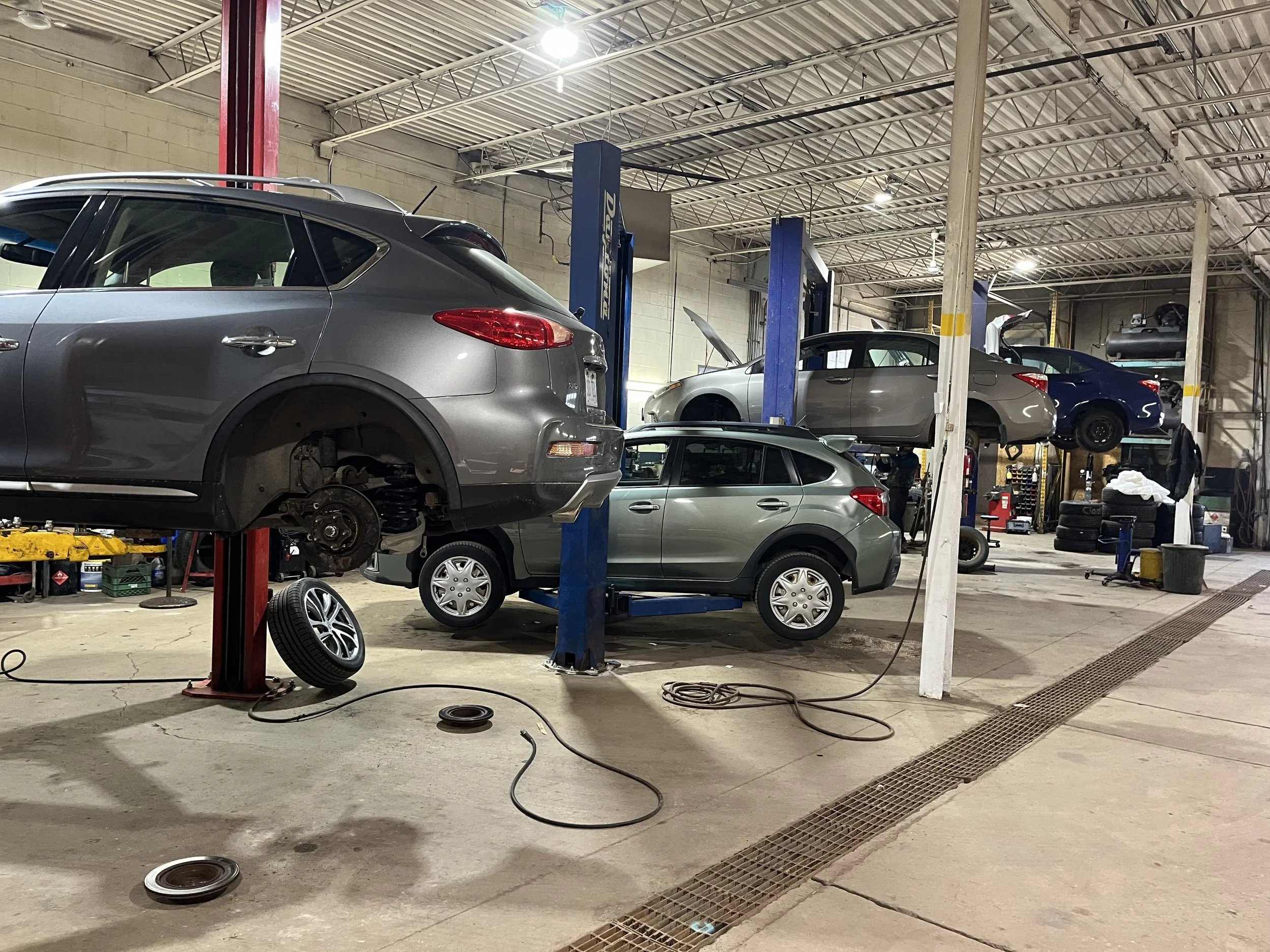 An automotive repair shop with multiple cars on lifts, some with wheels removed, tools, and equipment visible around the workshop.