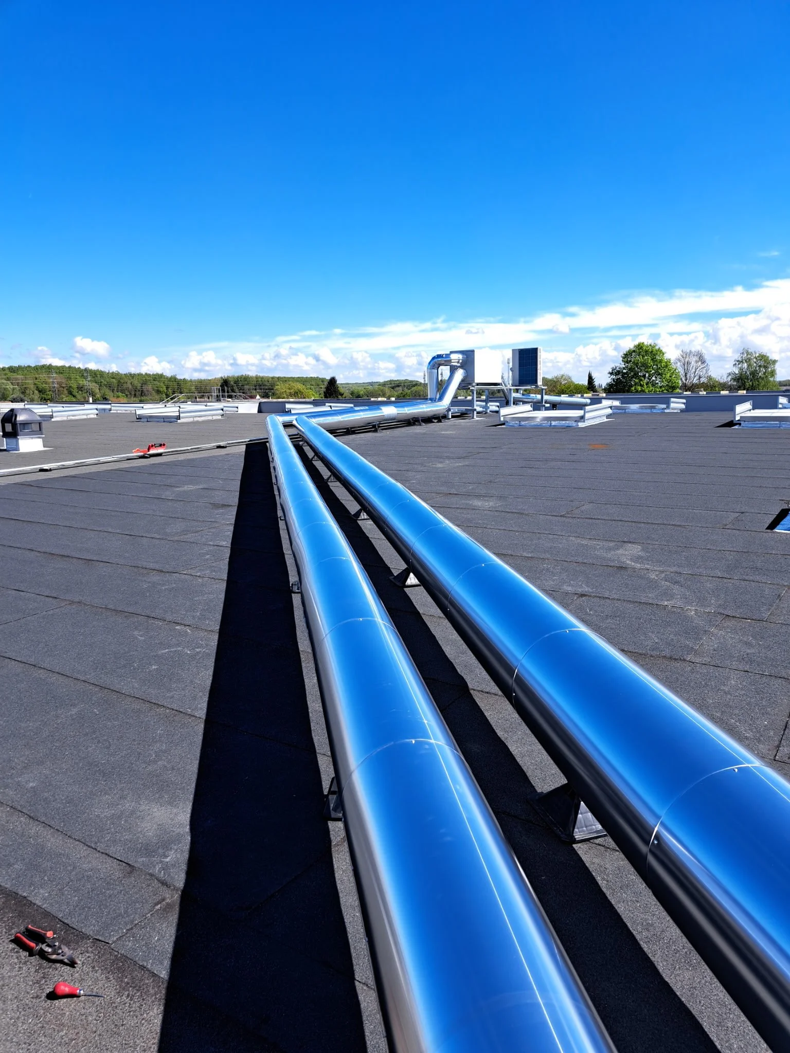Vue d'une toiture équipée de plusieurs systèmes de ventilation et de panneaux solaires contre un ciel bleu avec des nuages, avec des outils de réparation à l'avant-plan.