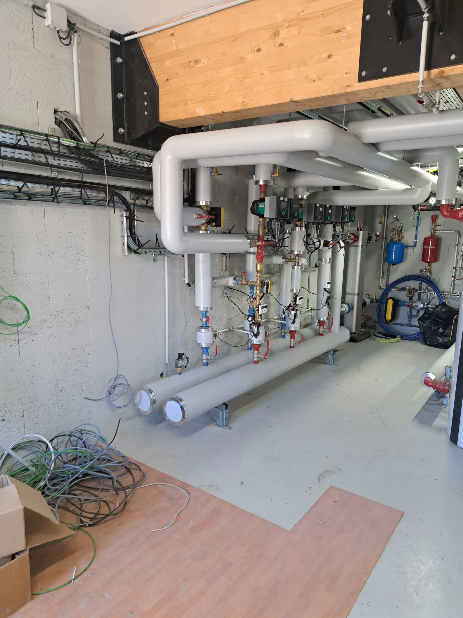 Installation de tuyaux et de câblages dans une pièce technique, avec des conduits en PVC, des vannes, et des éléments de raccordement, en cours de préparation.