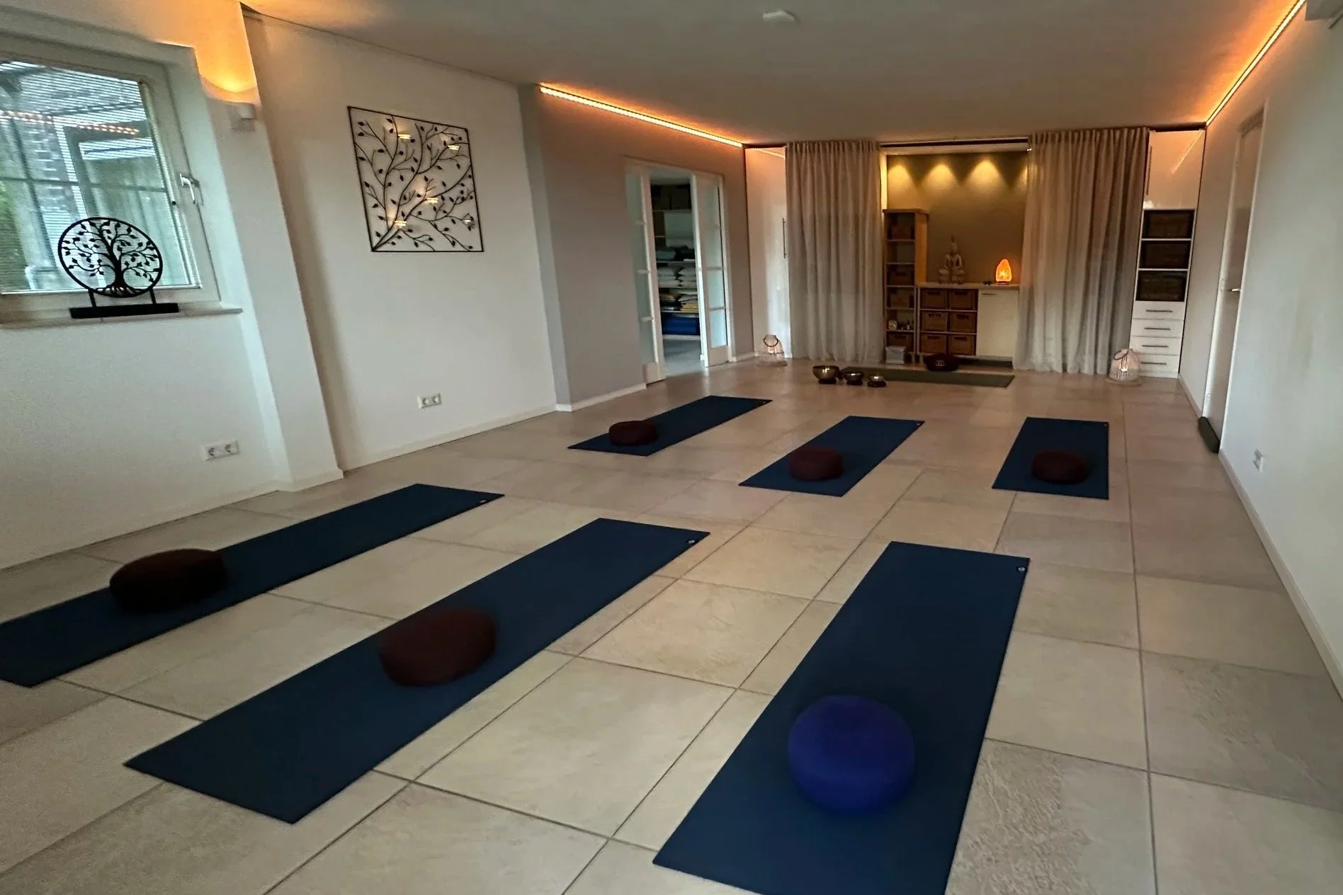 Binnenruimte ingericht voor yoga of meditatie, met matten, blokken en kussens op de vloer, sfeervolle verlichting en decoraties.