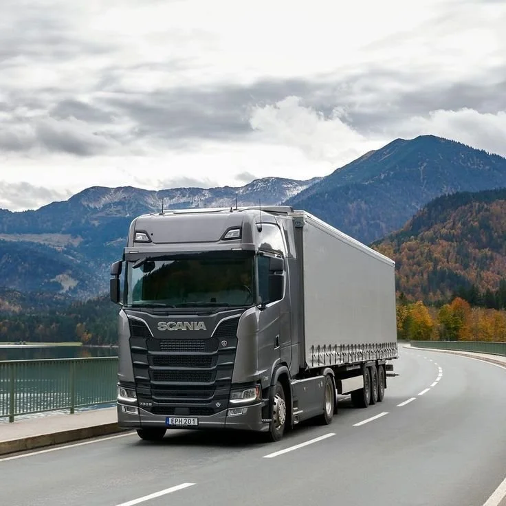 Ein schwarzes LKW fährt auf einer kurvigen Straße mit Bergen im Hintergrund.