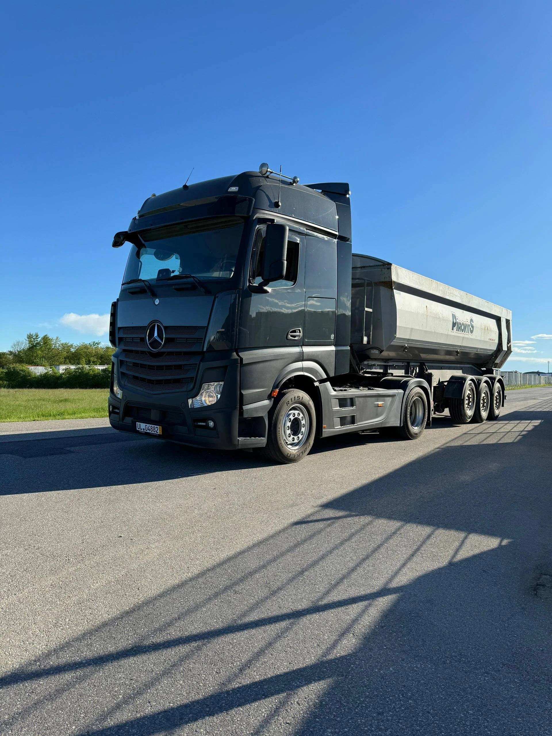 Schwarzer Mercedes-Benz LKW mit Anhänger auf einer Straße bei sonnigem Himmel.