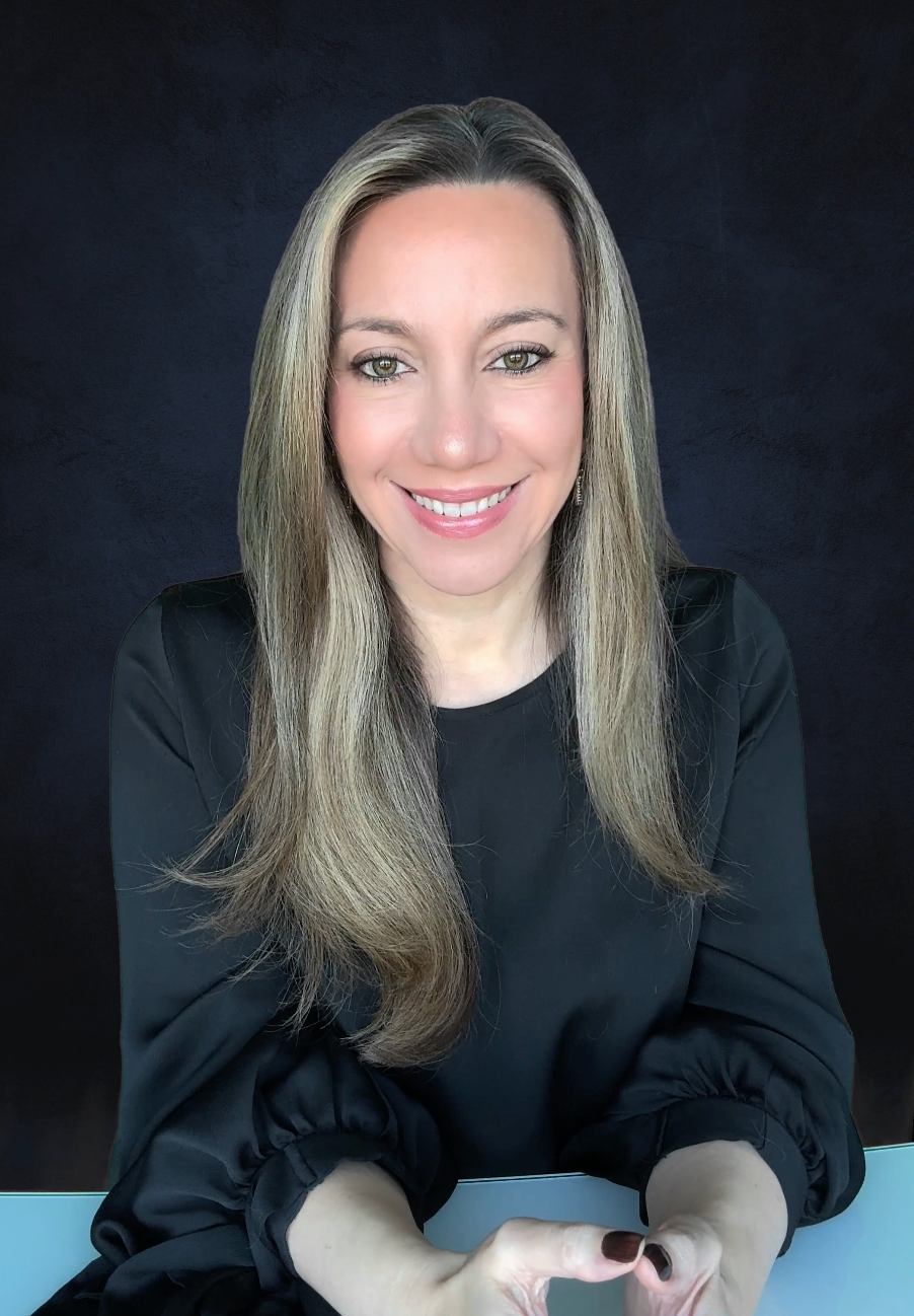 A woman with long blonde hair, smiling, wearing a black top, with a dark background.