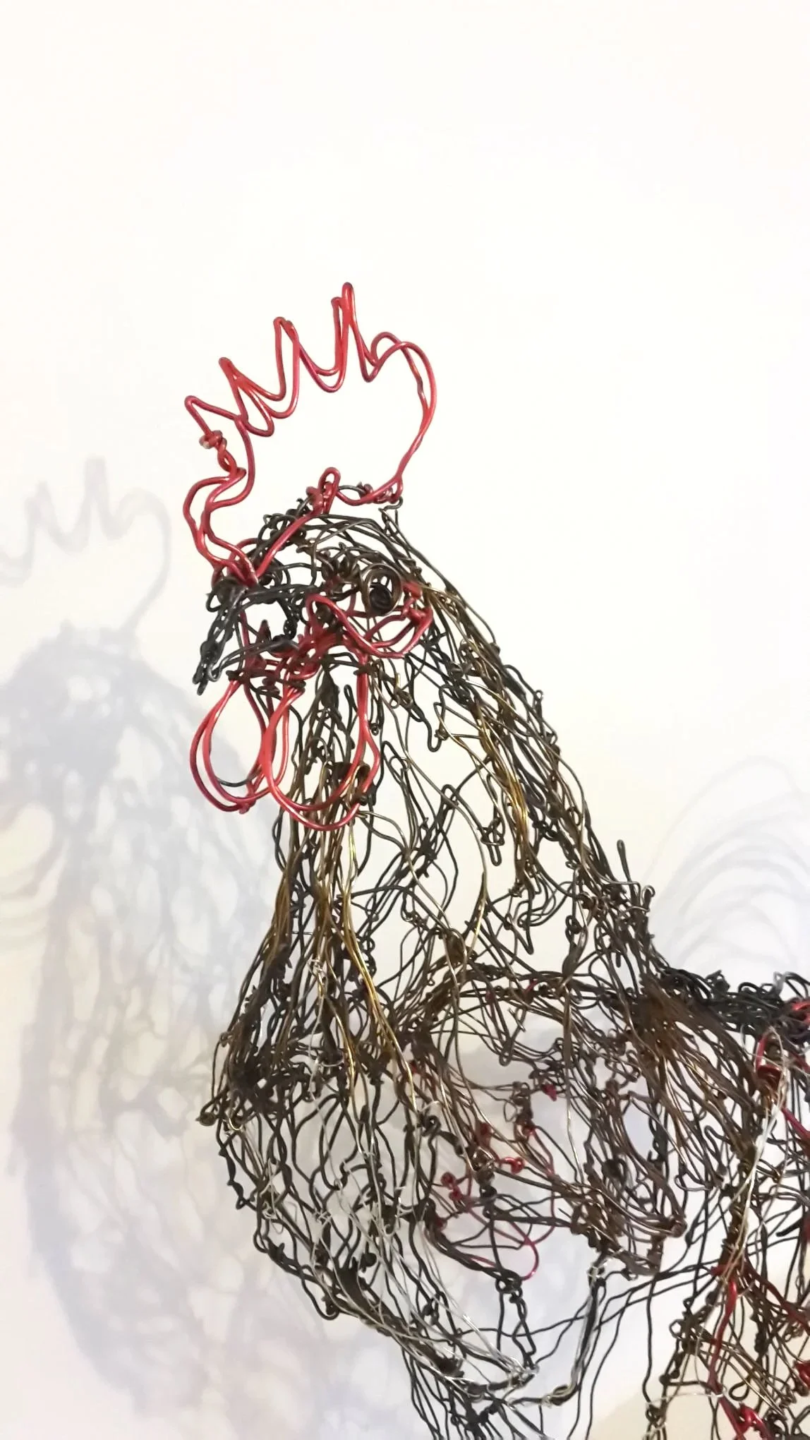 Statue en fil de métal représentant un coq, avec une crête rouge en fil de couleur rouge et noire.