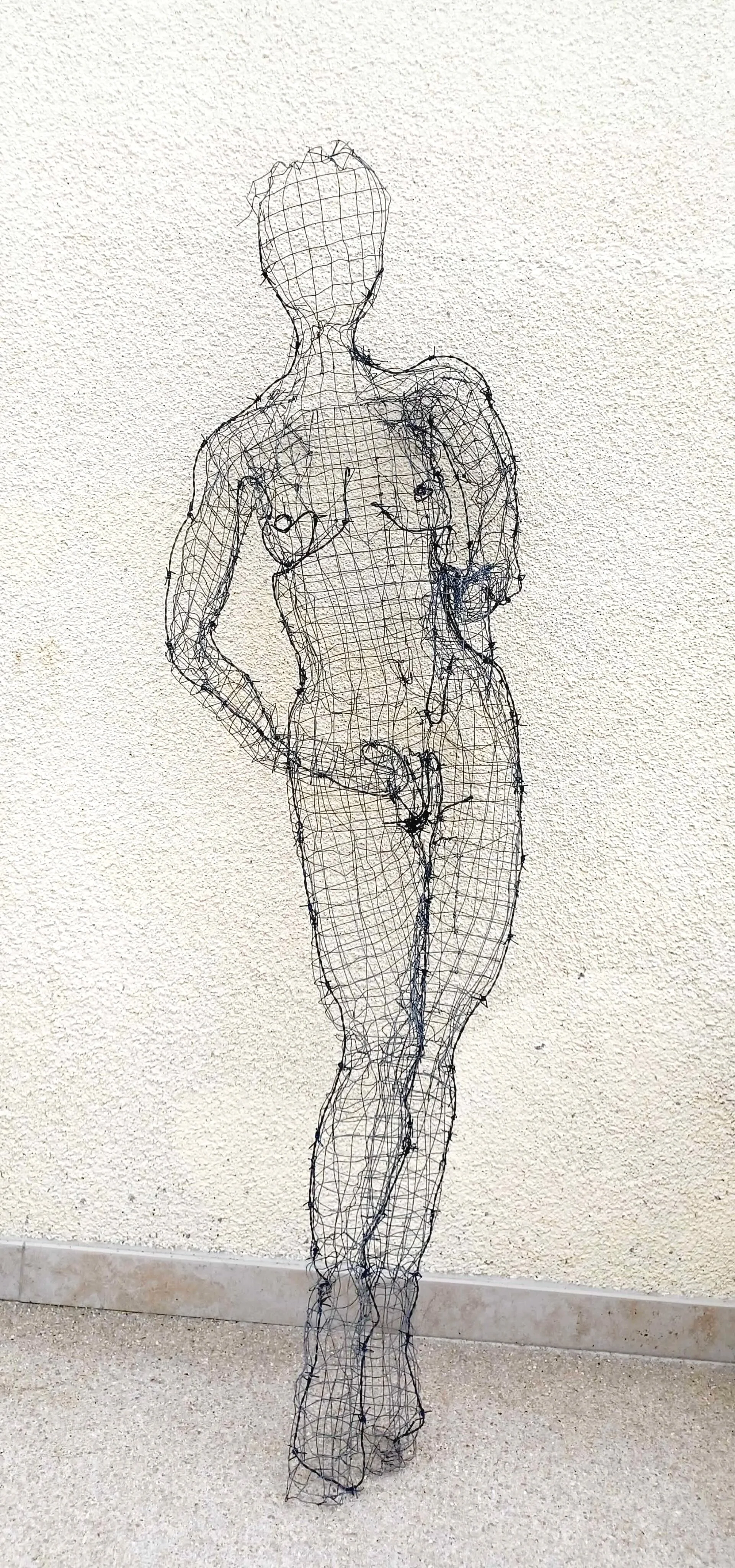 Sculpture d'une femme debout en grillage et fil barbelé