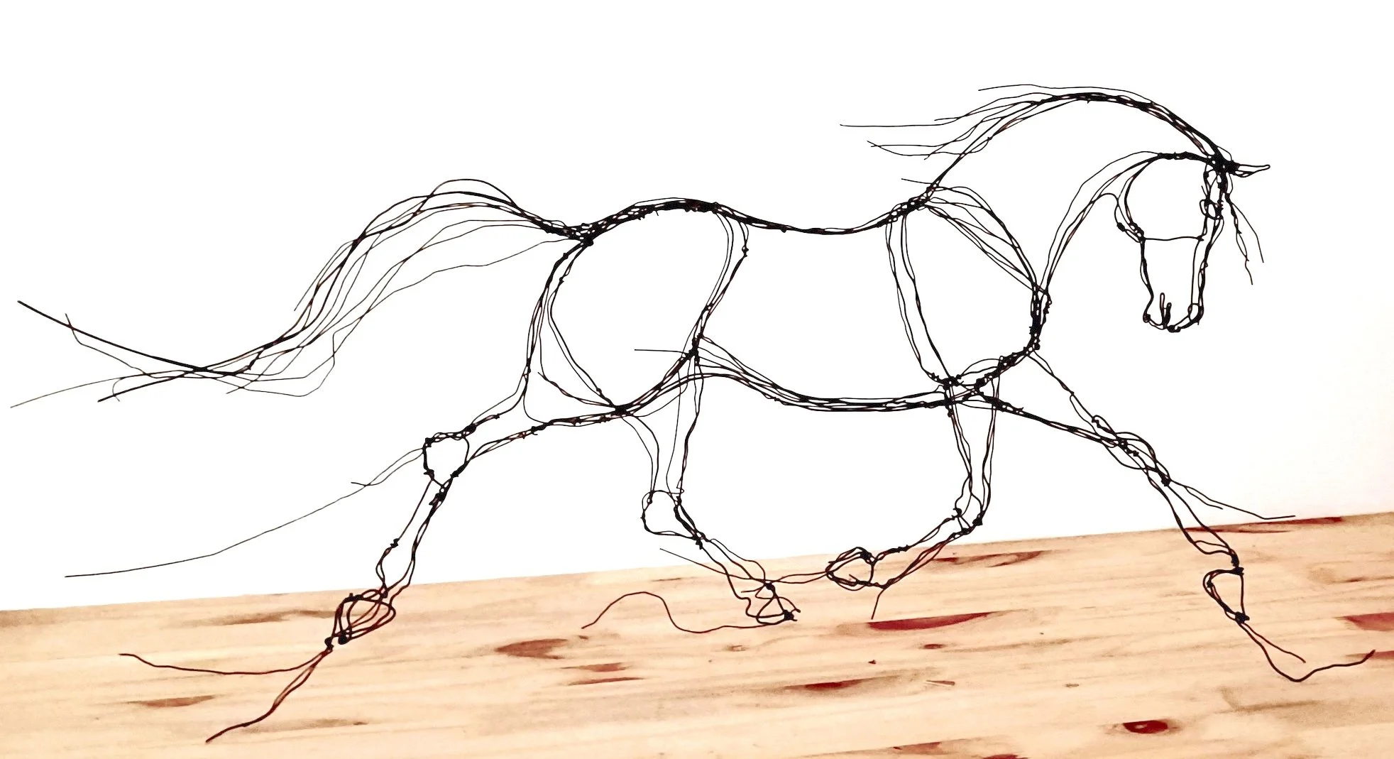 Sculpture en fil de fer représentant un cheval en mouvement, posé sur une planche en bois.