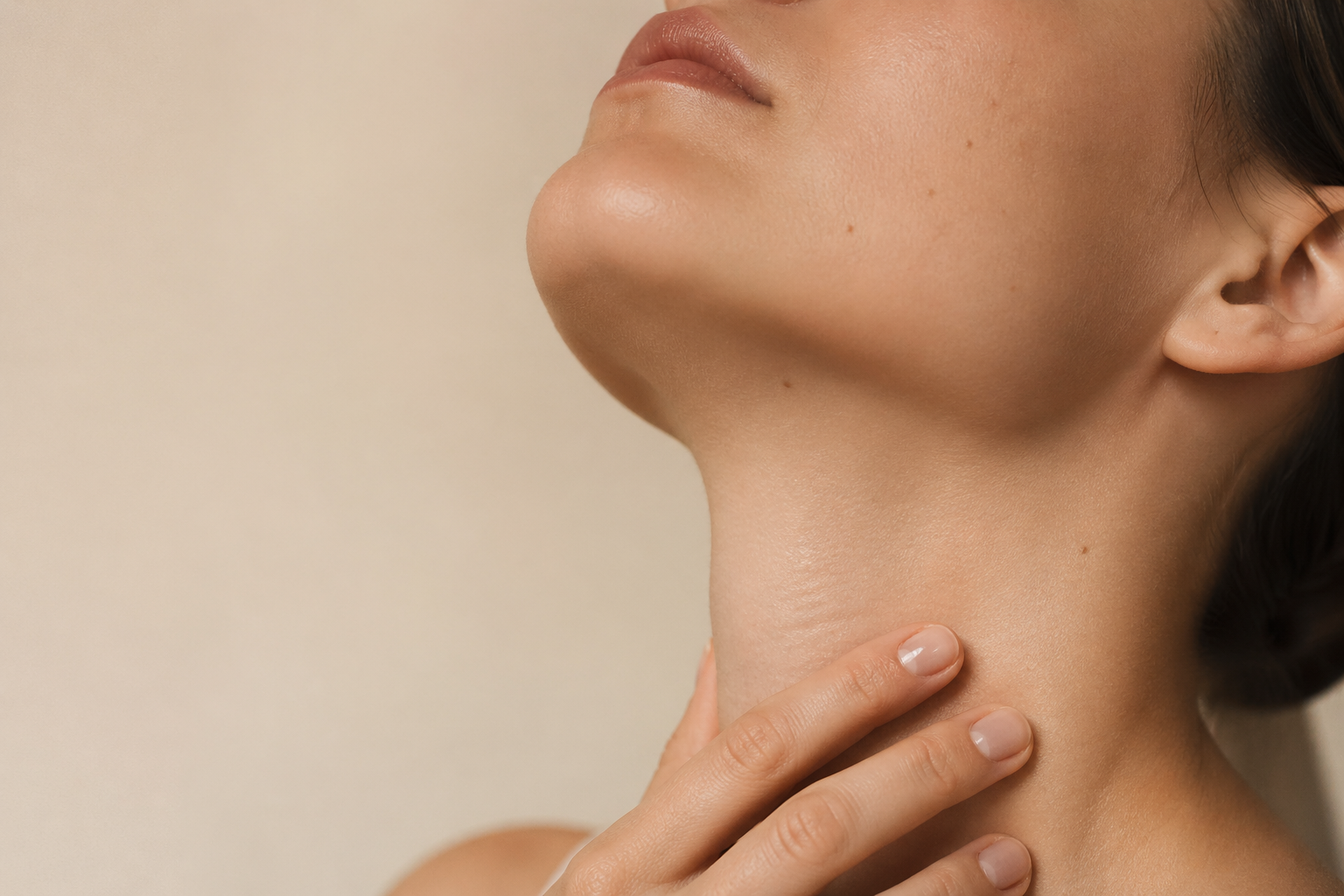 Close-up of a woman's lower face, chin, and neck, with her hand gently touching her neck.