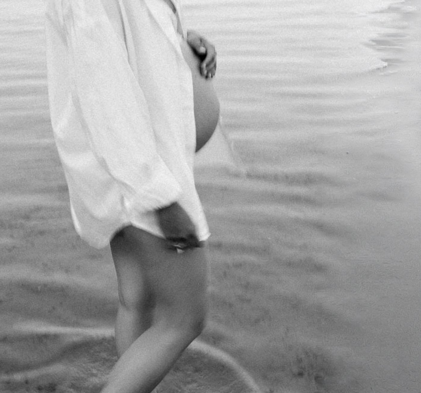 A person wearing a white shirt wading in shallow water at the beach, their legs partially submerged and their right hand hanging loosely by their side.