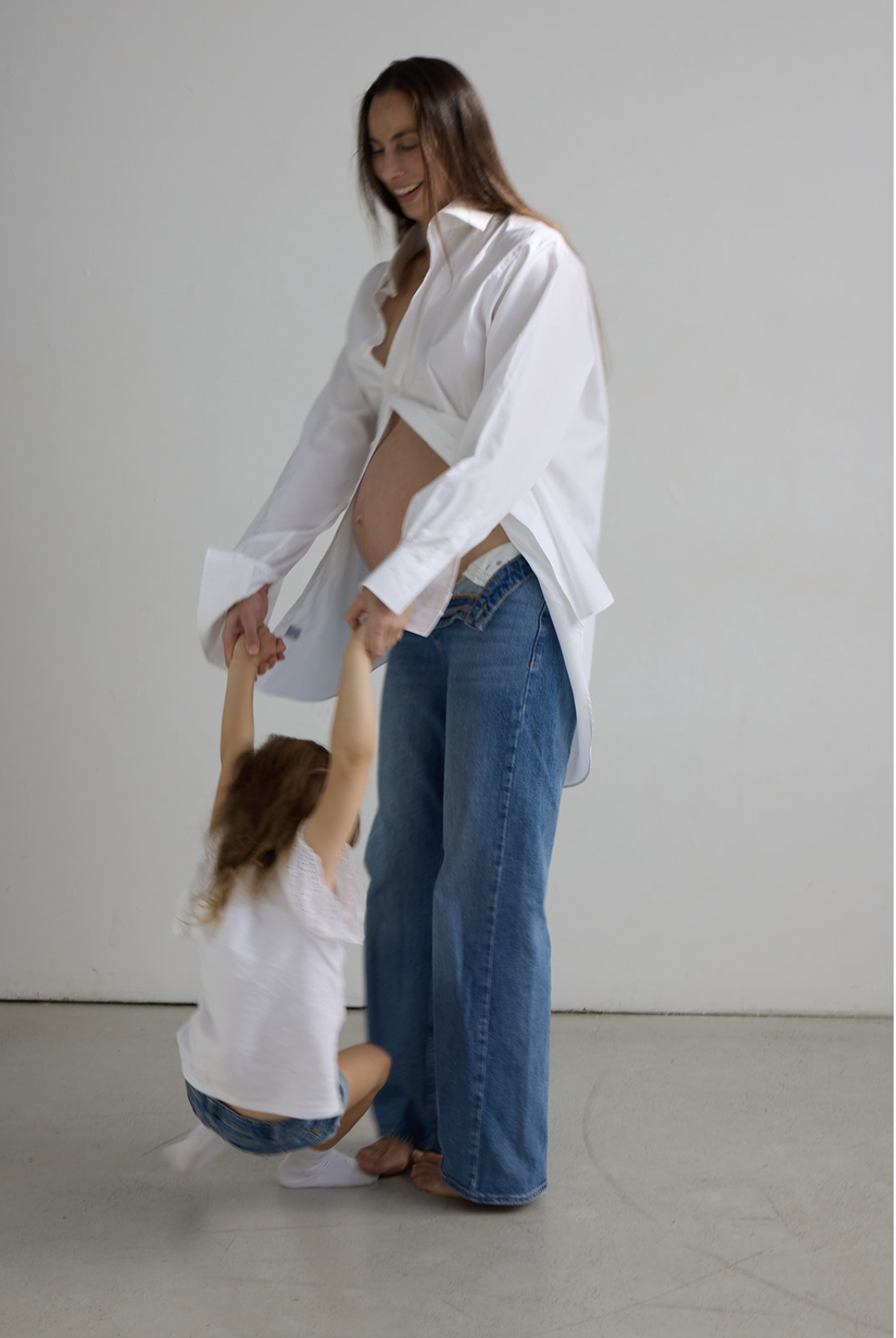 Woman in a white shirt and jeans holding hands with a young girl, who is jumping up and down.