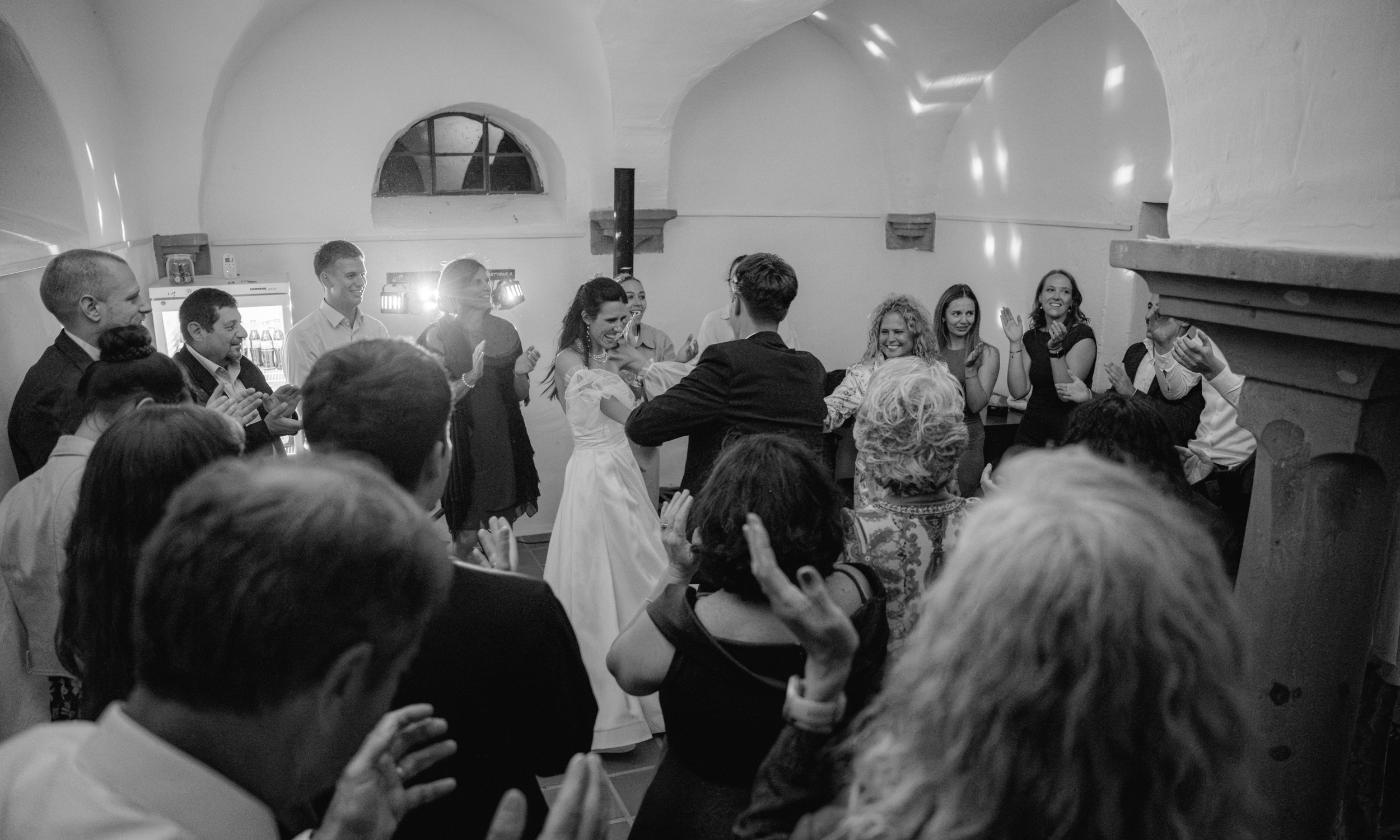 Mehrere Menschen tanzen und feiern in einem Raum, vermutlich bei einer Hochzeit, während alle fröhlich lachen und sich umarmen.