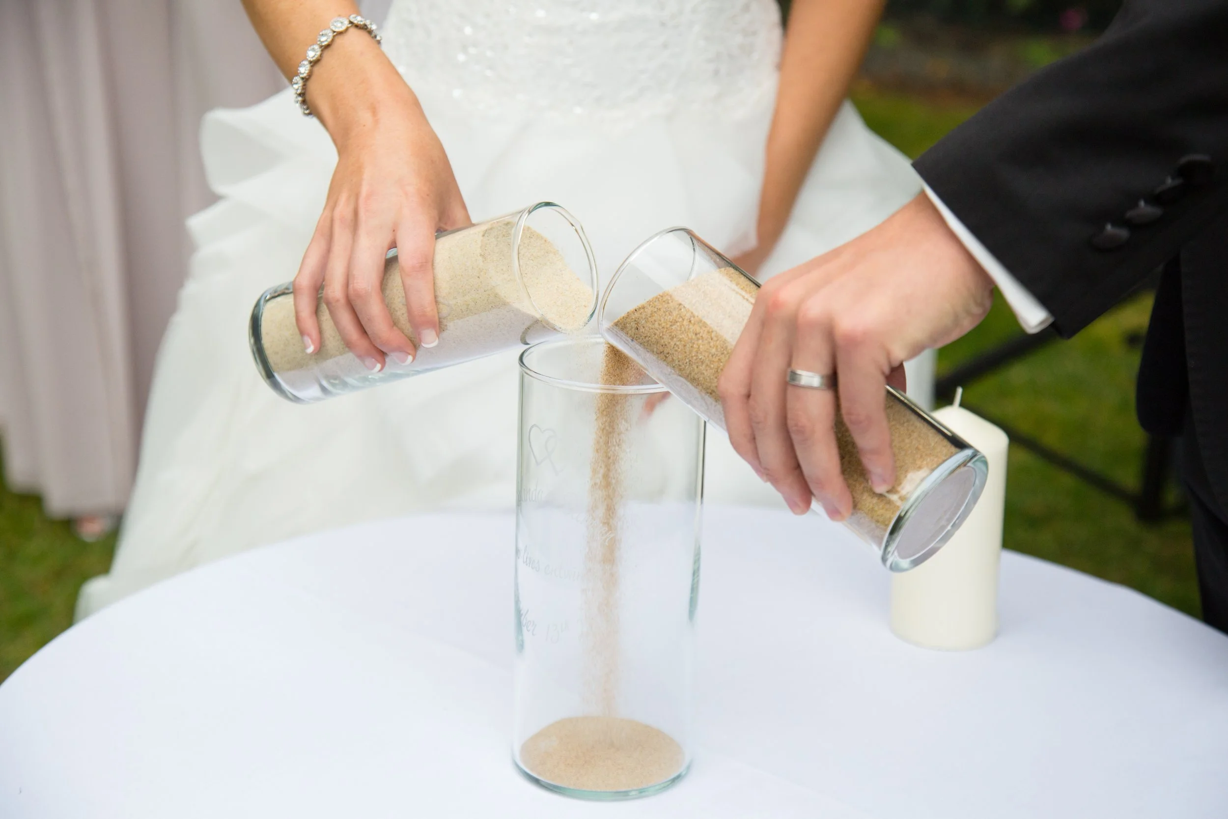Wedding ceremony where bride and groom are pouring sand from separate containers into a single glass container, symbolizing unity.