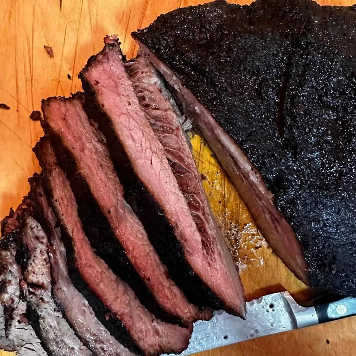 Slices of smoked brisket on a wooden cutting board with a dark bark exterior.