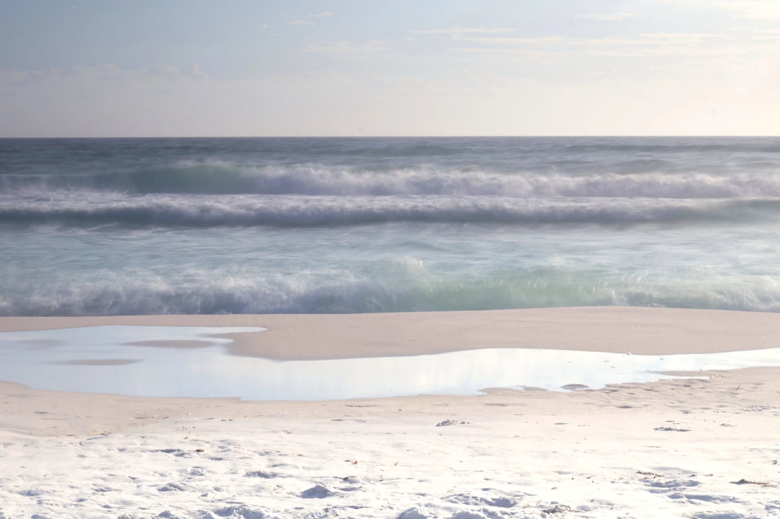 Empty sandy beach with ocean waves and a partly cloudy sky in the background.