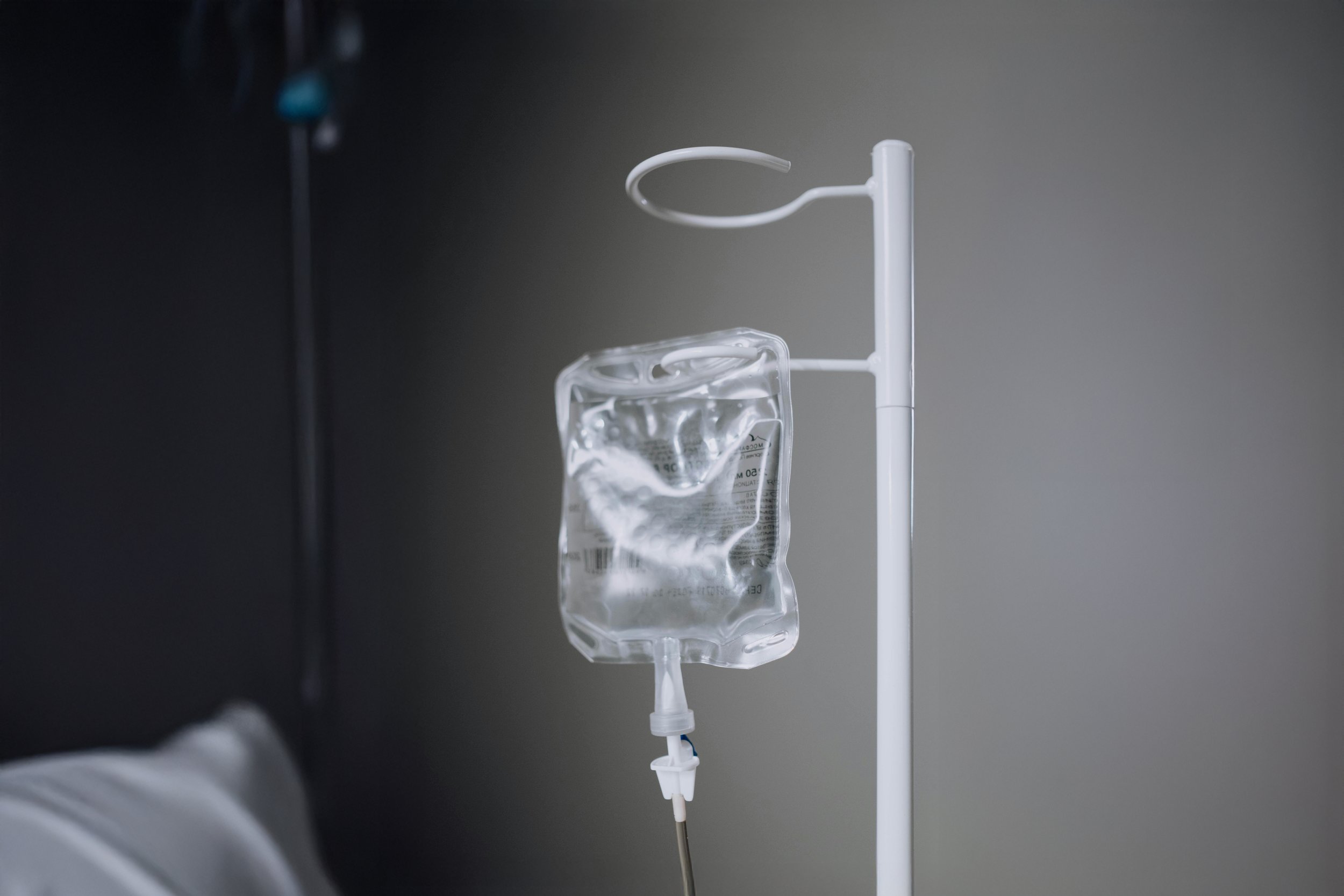 Medical IV drip with a clear fluid bag hanging from a white stand in a clinical setting.