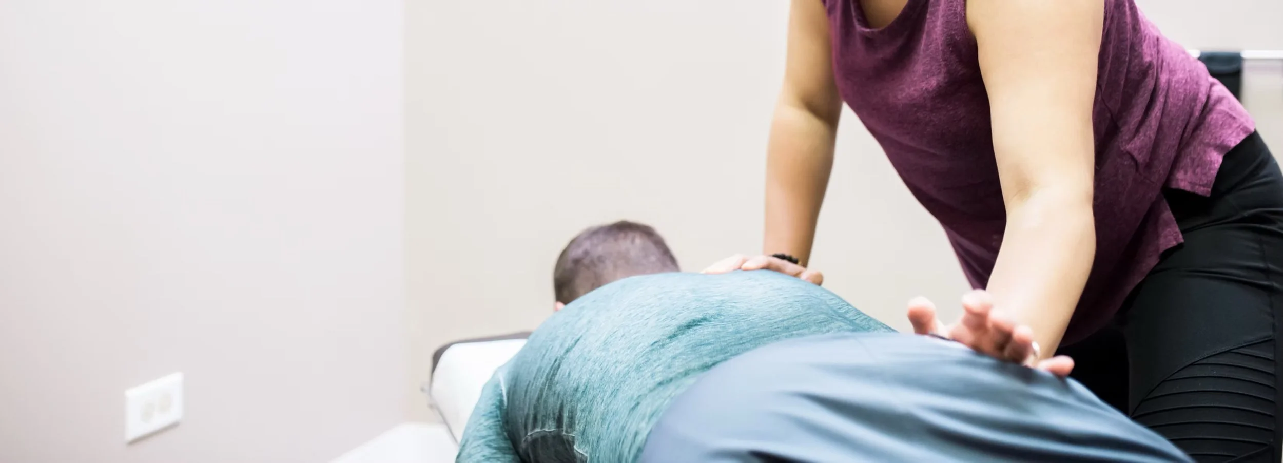 Physical therapist providing back massage to a patient lying face down on a treatment table.