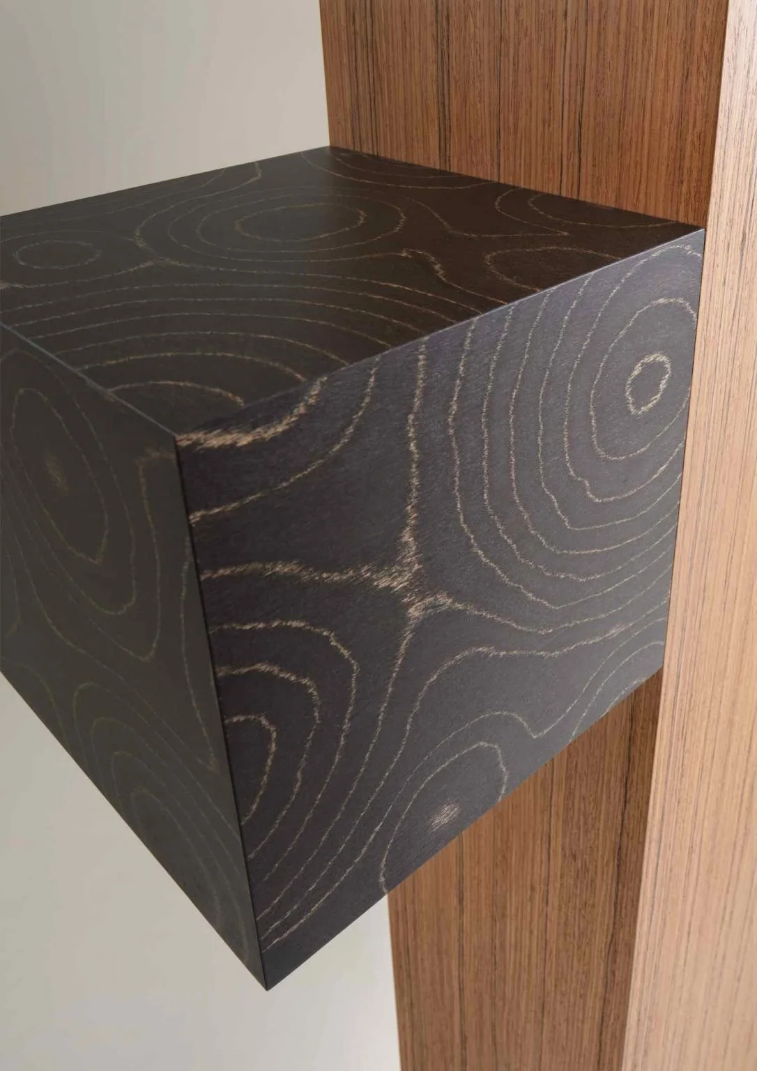 Close-up of a black wooden cube with wood grain patterns, mounted on a wooden surface.