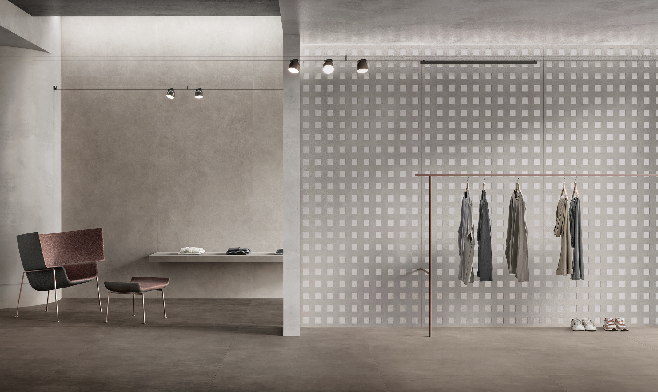 Modern minimalist room with a chair, a desk, and a clothes rack holding hanging clothes, with a half wall separating the two areas.