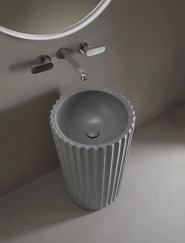 Modern bathroom sink with a unique, ribbed cylindrical design and a round basin, paired with sleek wall-mounted faucets and a mirror above.