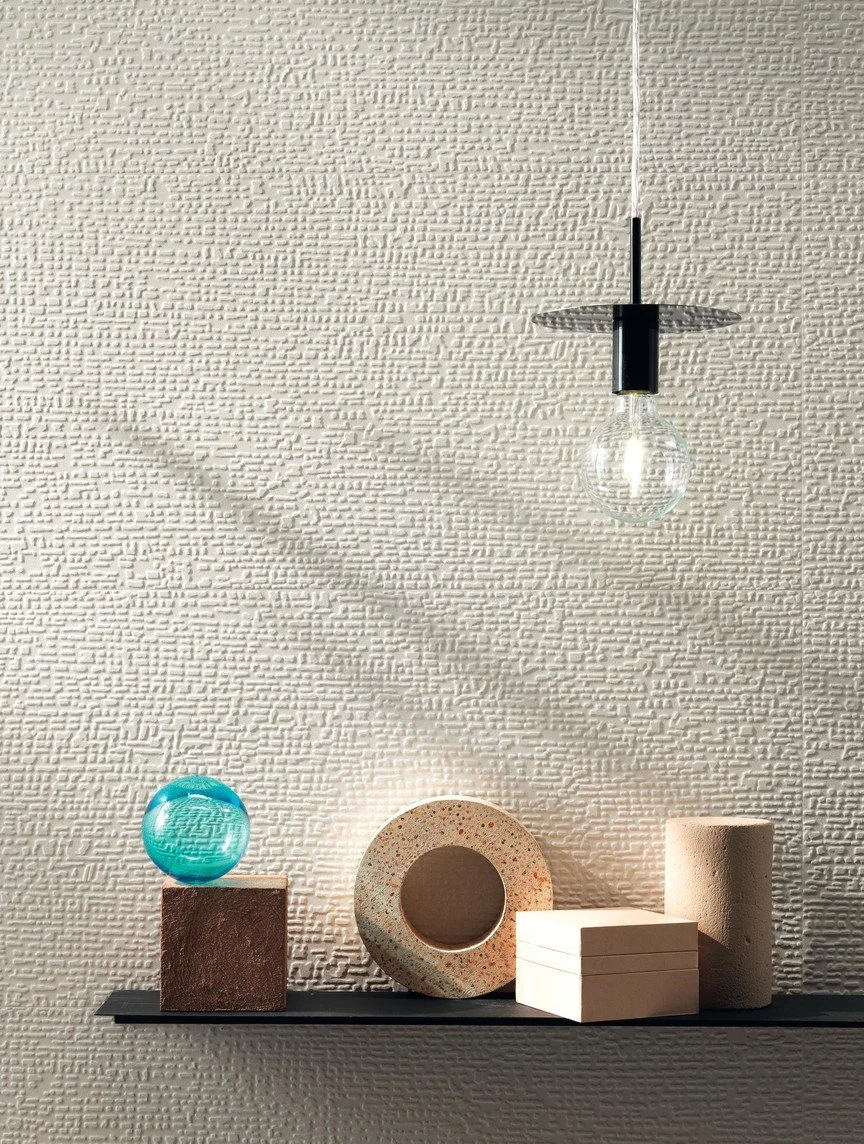 Decorative objects on a black shelf against a textured white wall, including a glass orb, a circular stone sculpture, and stacked rectangular blocks.