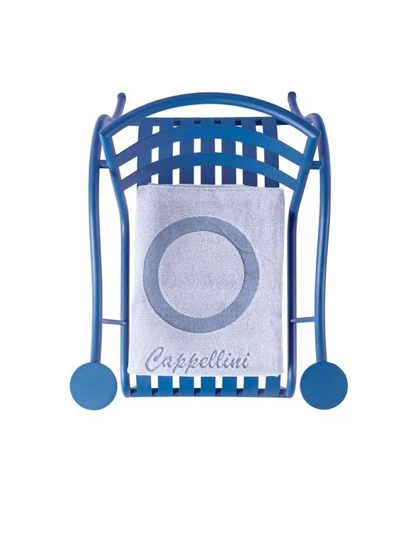 A blue plastic chair with a white towel draped over it featuring a gray circle and the word 'Cappellini' embroidered on it.