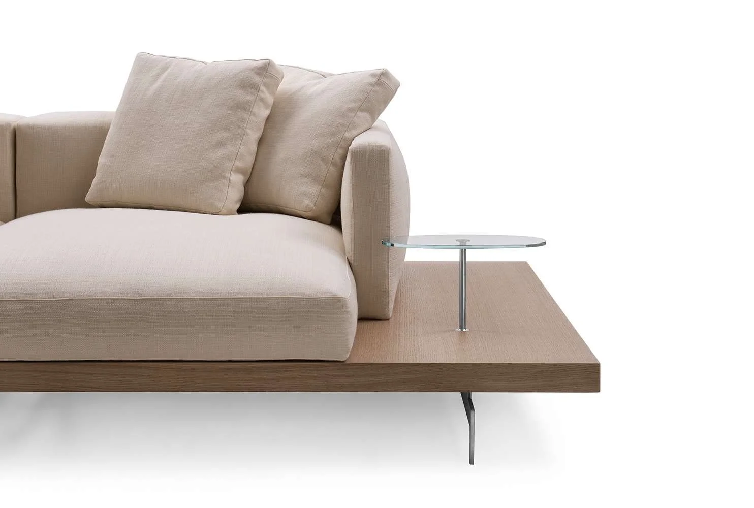 Close-up of a beige sofa with two matching cushions, a wooden platform, a small glass side table, and a beige rug on a white background