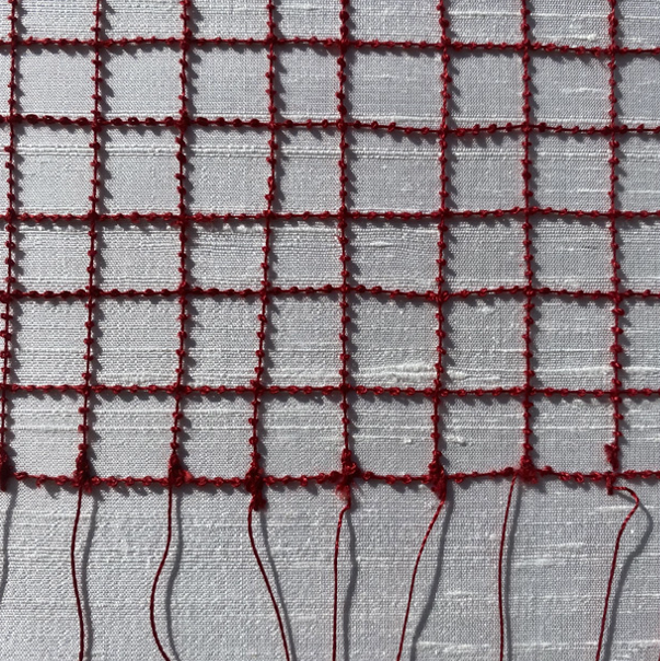Close-up of a red wire grid attached to a white fabric background.