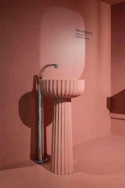 Pink pedestal sink with fluted design next to a matching wall and a sleek silver faucet.