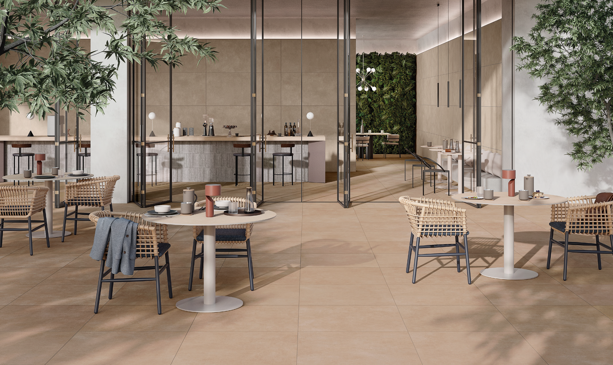 Modern, stylish hotel restaurant with a neutral color palette, featuring round tables with chairs, decorative vases, and a glass partition separating the dining area from a bar or lounge space with high stools. Green plants and a textured green wall 