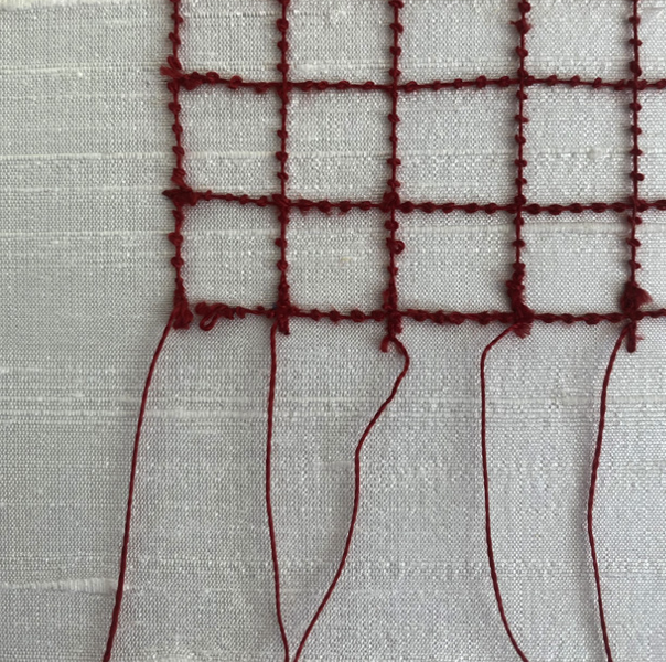 Close-up of red embroidery stitches forming a grid pattern on white fabric.