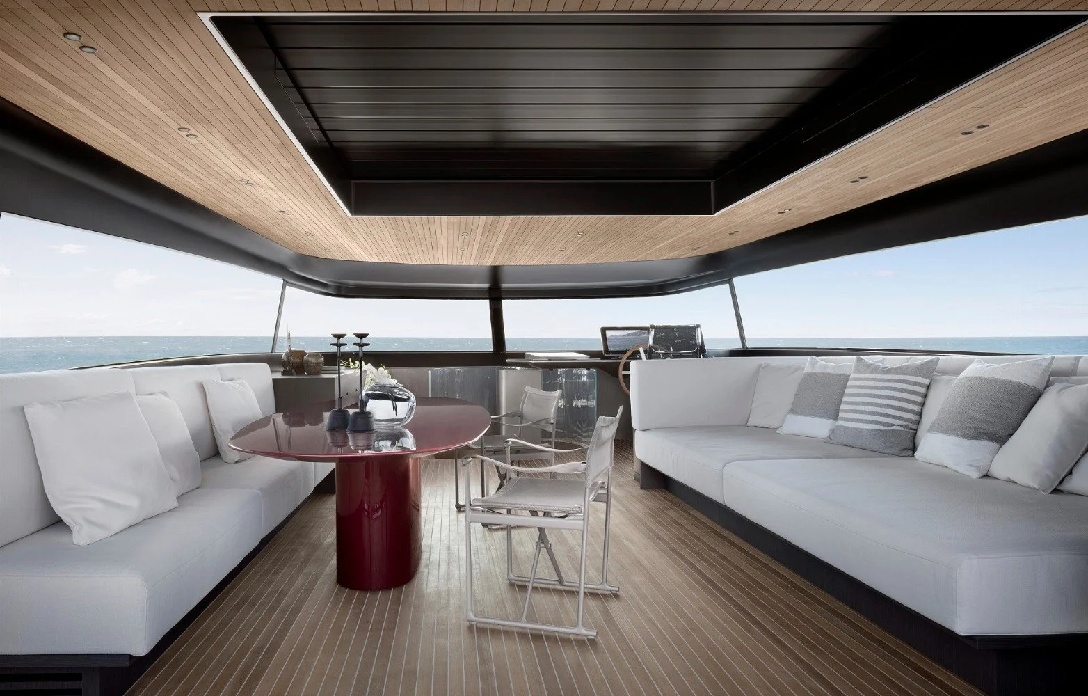 Luxury yacht interior with white couches, a red dining table, and ocean view through large windows.