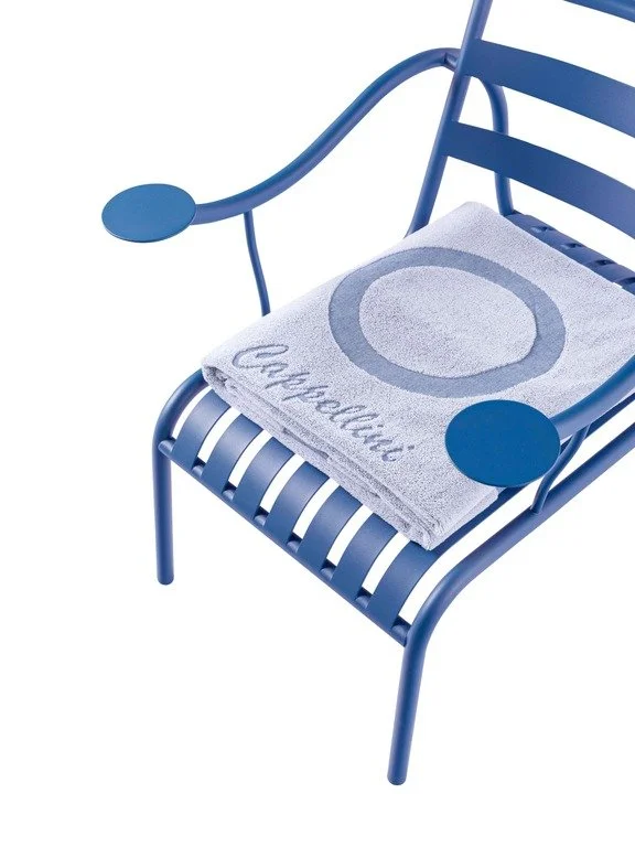 Blue outdoor chair with a towel on it that has a circular design and the word 'Coucou' embroidered on it.